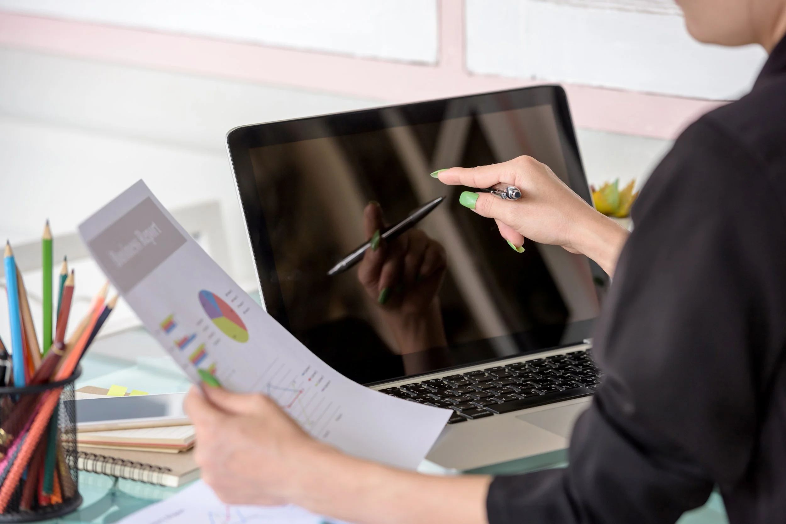 A person working at a desk, holding a printed chart and using a stylus with a tablet computer.