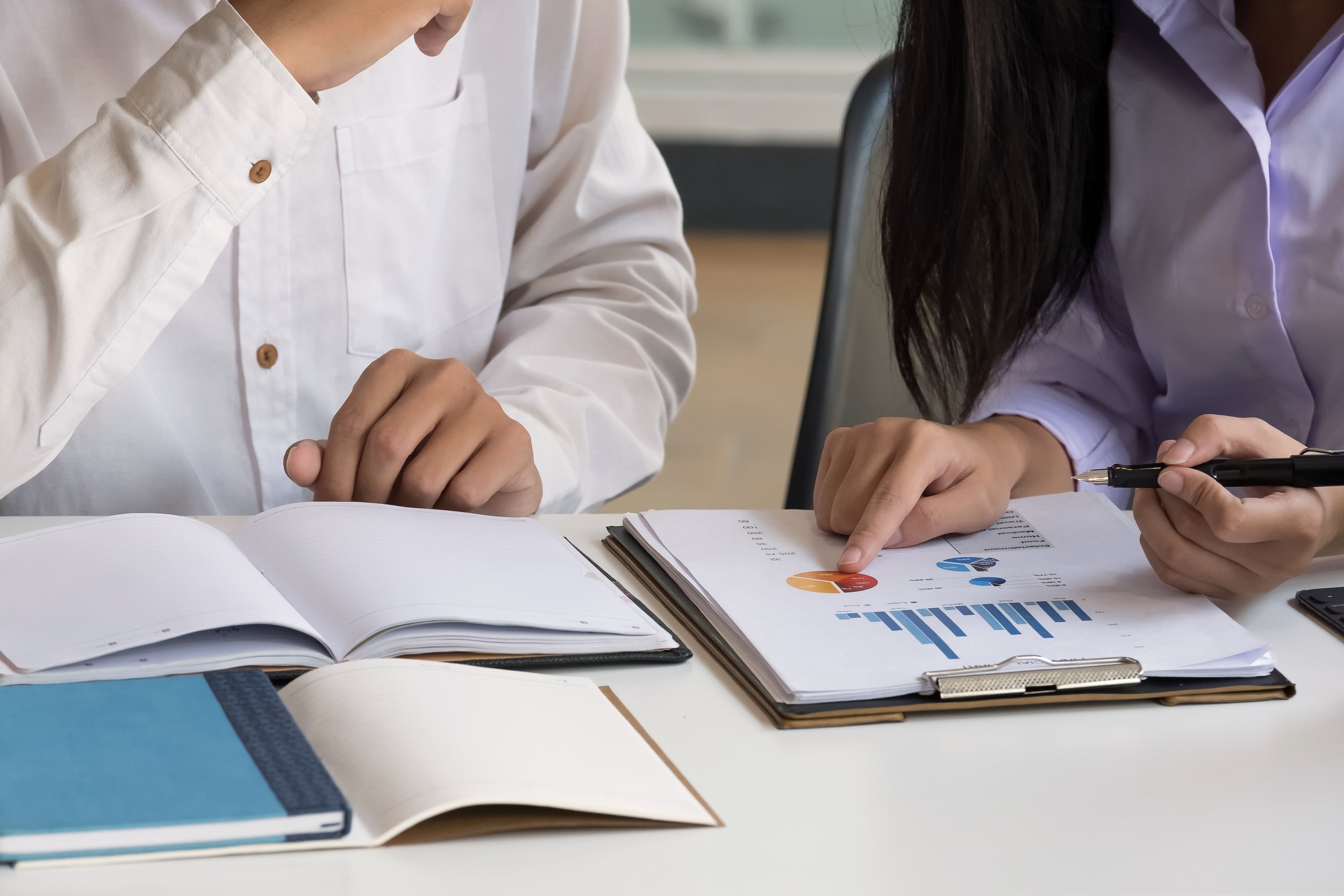Two people analyzing financial documents and data charts at a meeting.