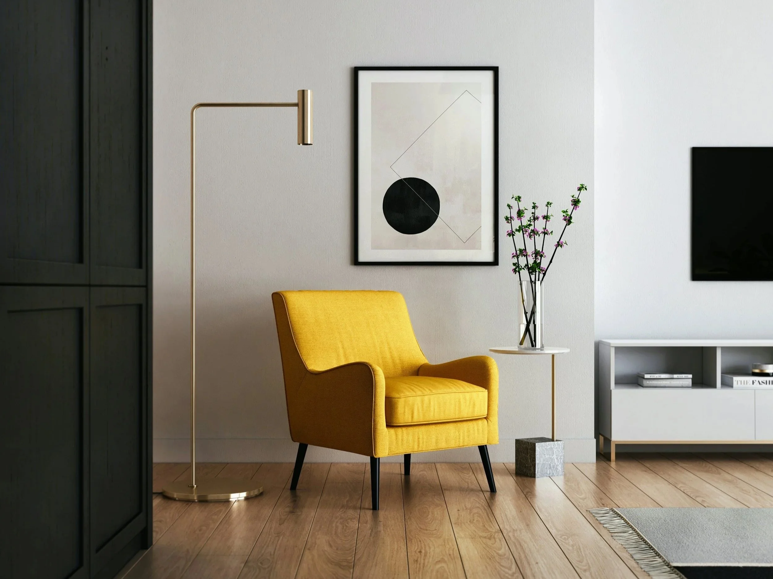Modern living room corner with a yellow armchair, a small side table, a tall gold floor lamp, a framed abstract art piece, a vase of pink and green flowers, and a white TV stand with books, on a wooden floor.