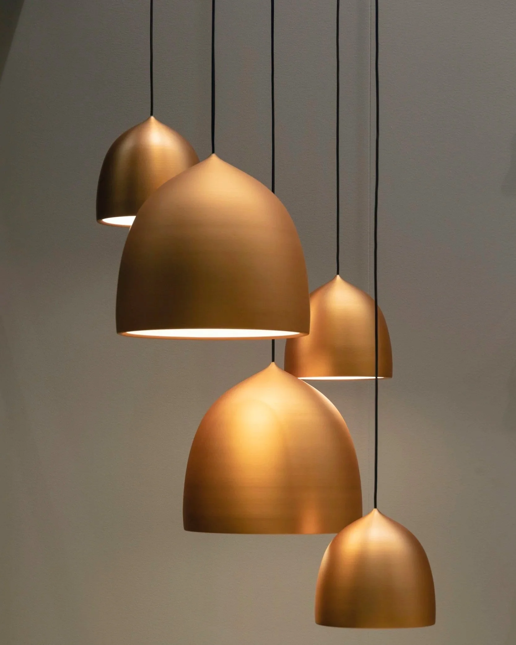 A modern pendant light fixture with five gold-colored domed shades hanging at different heights