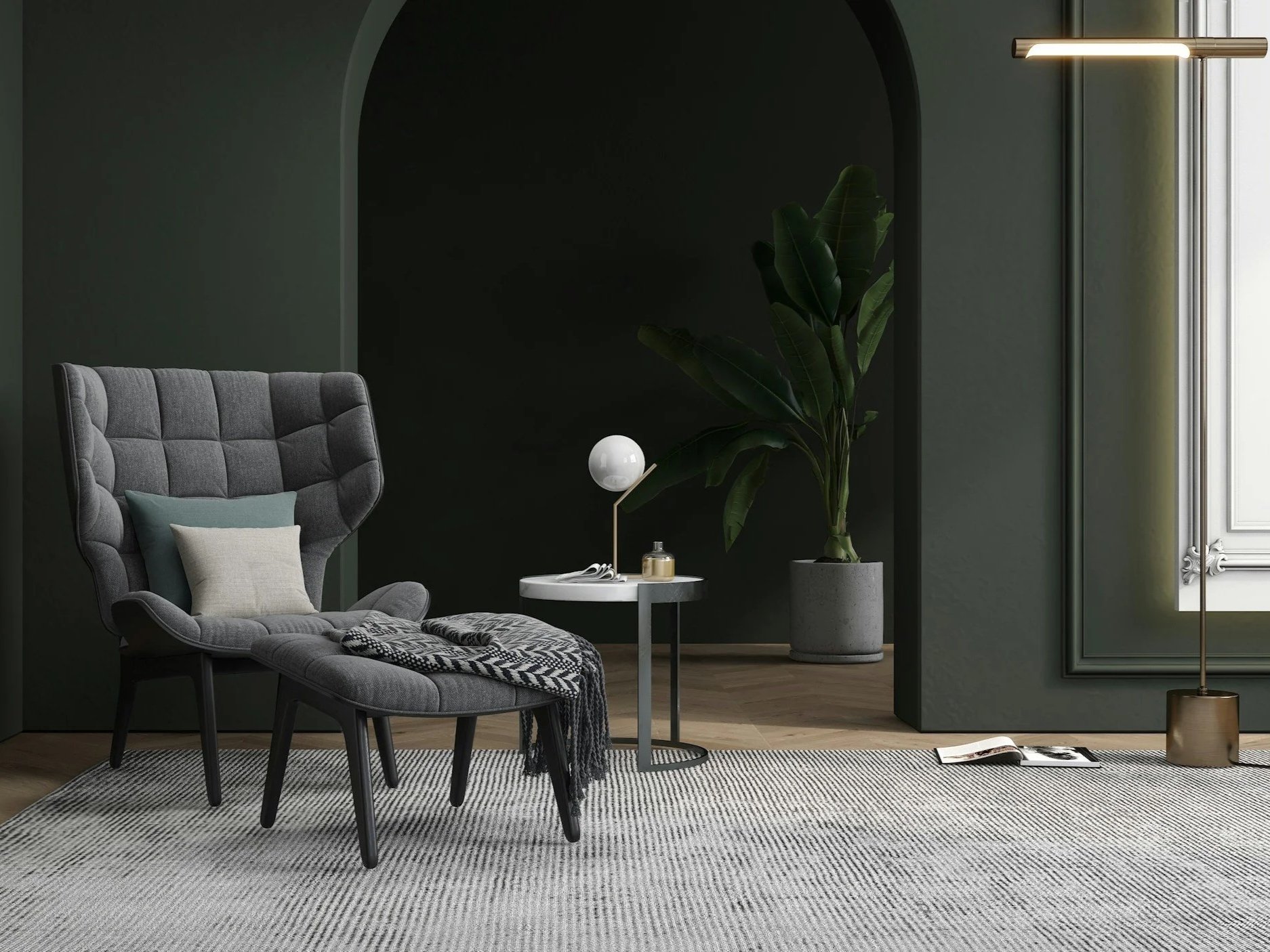 Minimalist living room with a gray high-back chair, a small round side table with a modern table lamp and decorative items, a large potted plant, and a window with a gold floor lamp beside it. The room has dark green walls and a light-colored rug.