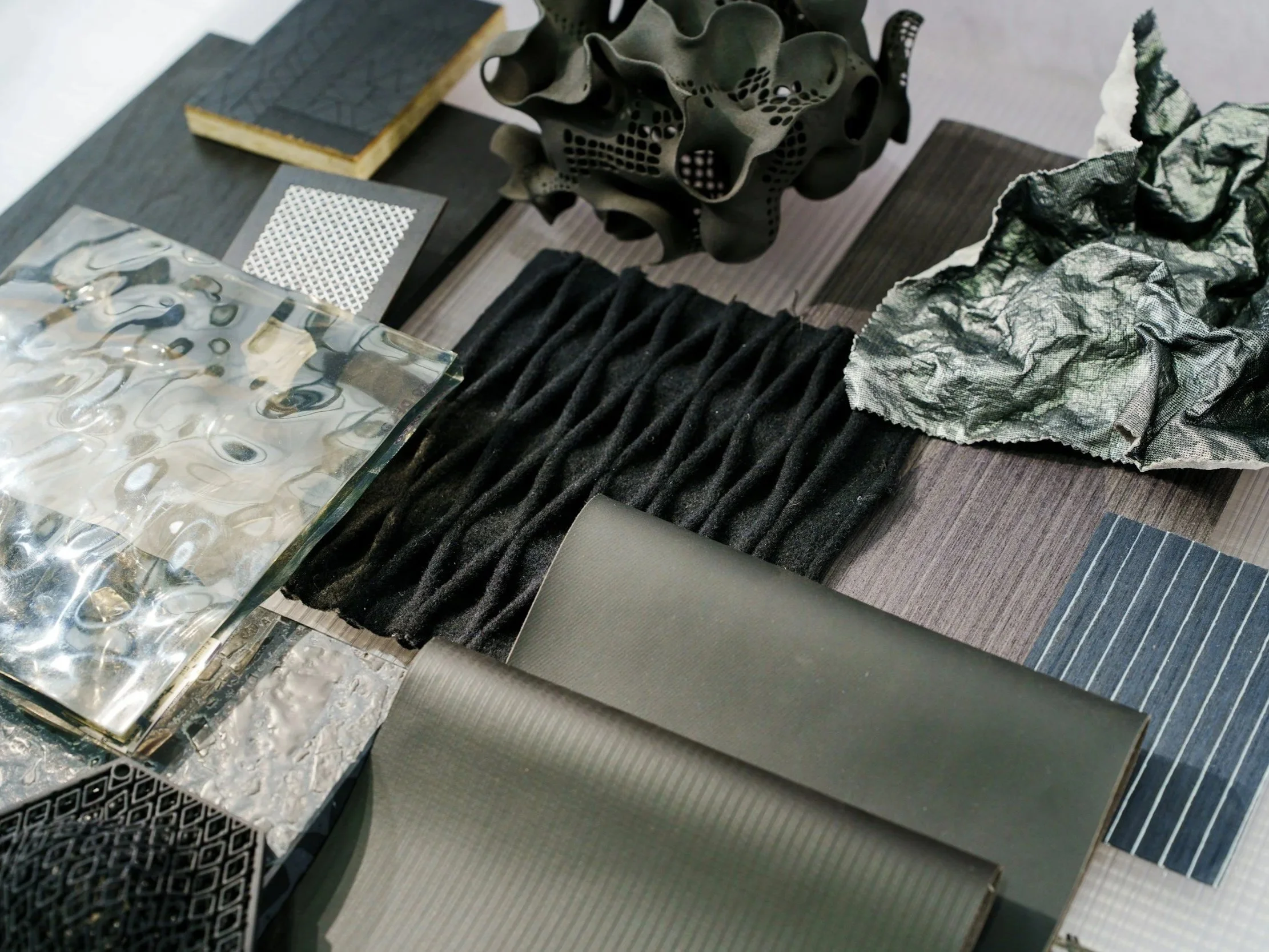 A collection of design and material samples including fabric swatches, textured papers, metal sheets, and decorative objects with abstract designs.