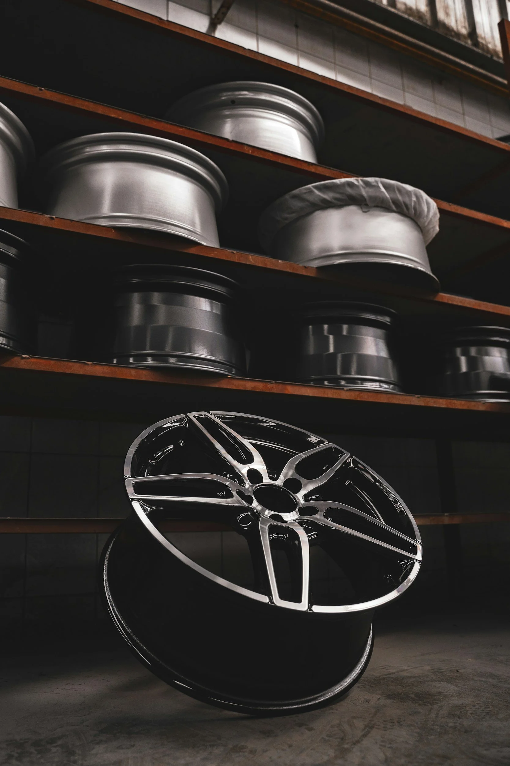 A car wheel rim lying on the concrete floor in front of a shelving unit with various metallic rims on the shelves.