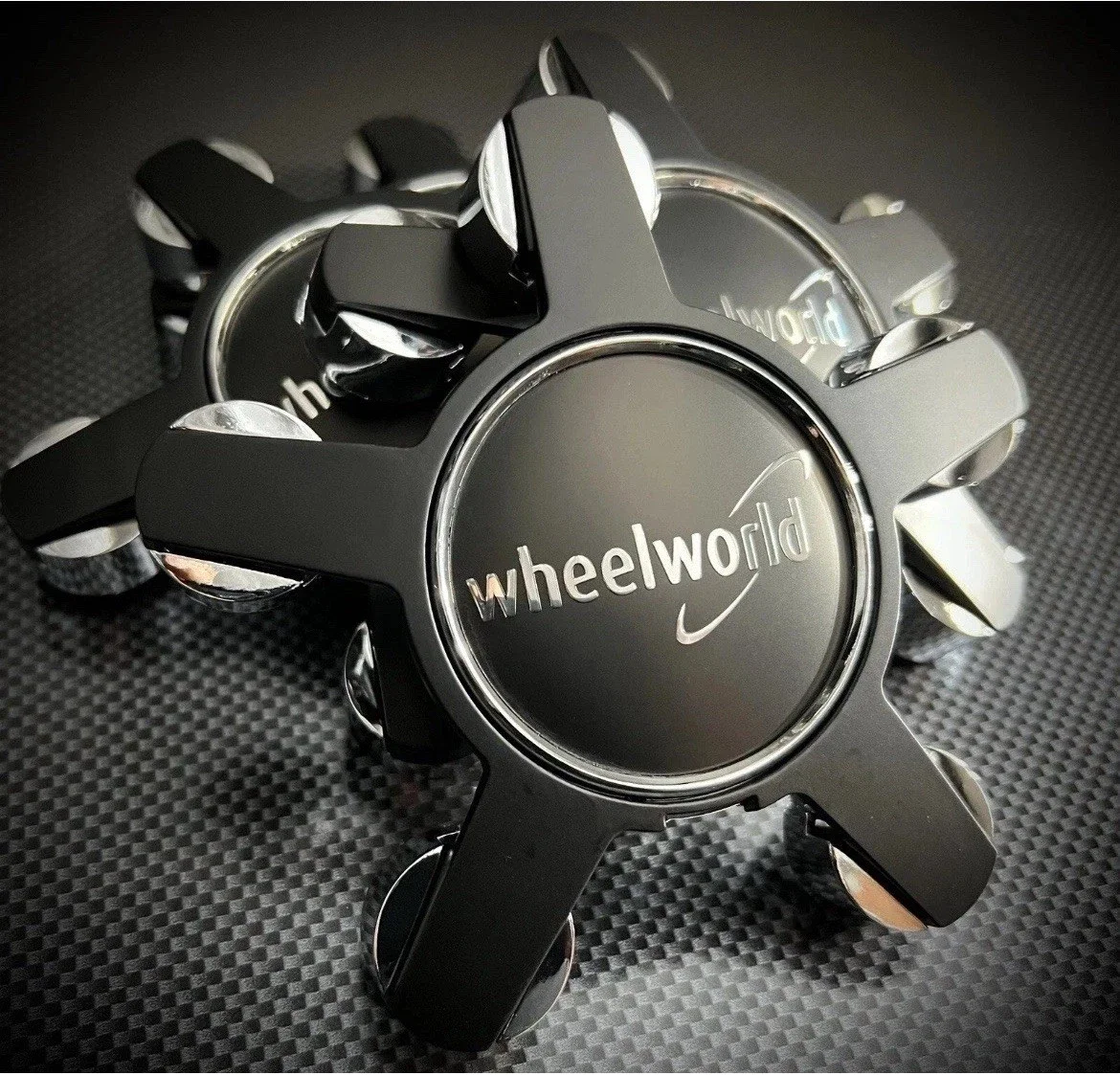 Close-up of multiple black wheel spacers with the Wheelworld logo on a textured black surface.