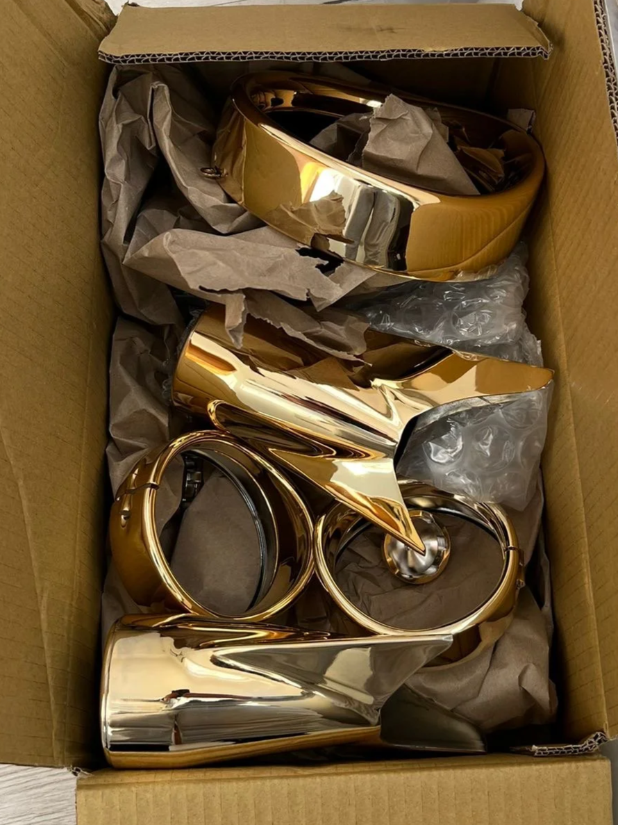 Gold-colored decorative letters spelling 'LOVE' inside a cardboard box with crumpled brown paper for protection.