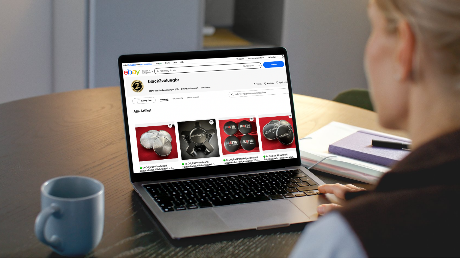 A person browsing eBay on a laptop, viewing listings for wheel covers and wheel accessories. The laptop screen displays the eBay seller page 'black2valuegr' with various wheel-related products.
