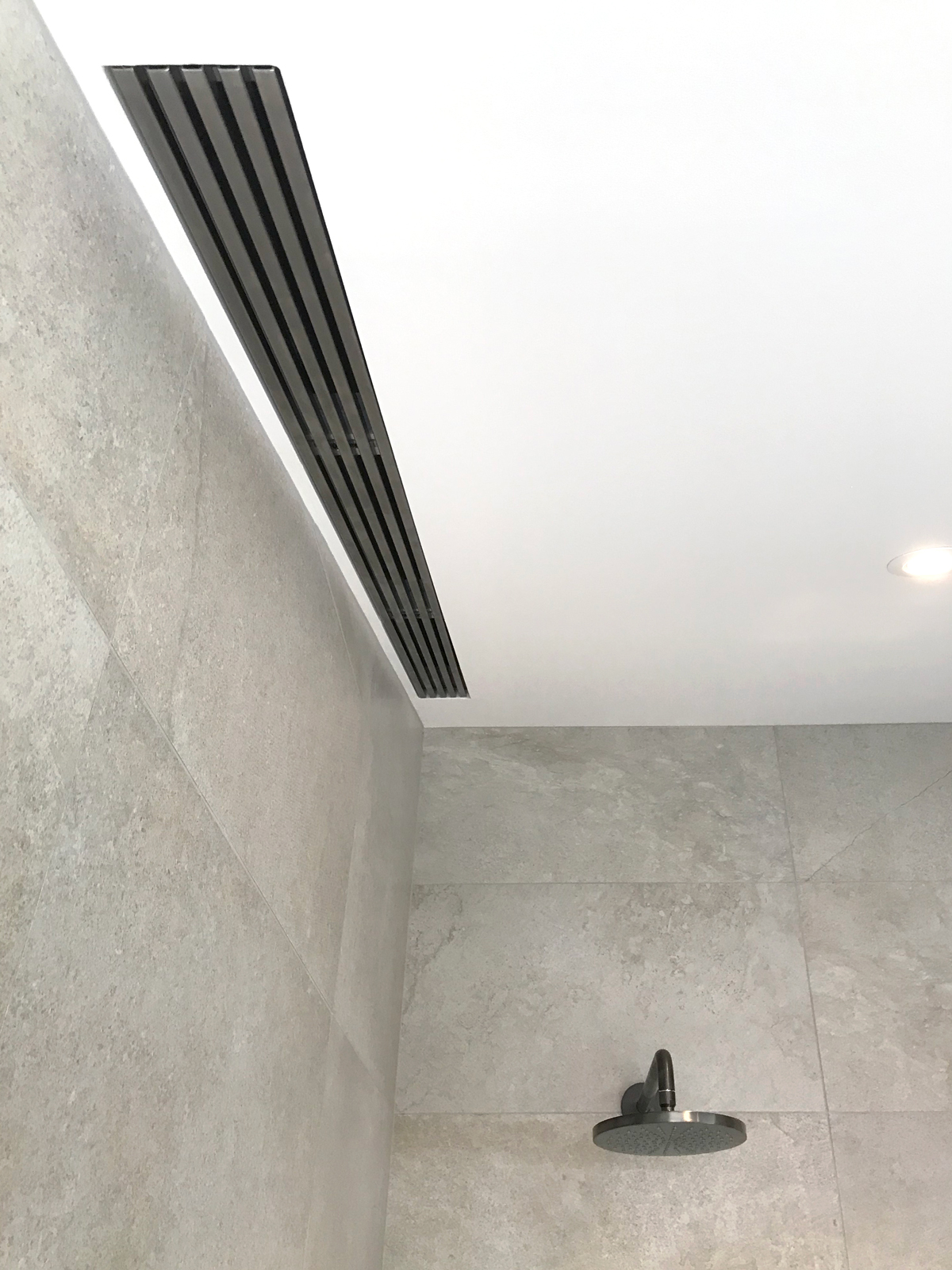 Modern shower with ceiling vent and gray tiles