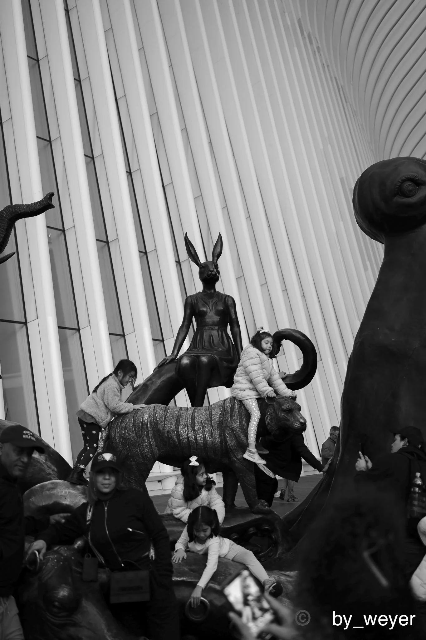 Children and adults interacting with a large animal sculpture of a tiger and other animals, in an indoor space with modern architectural design.