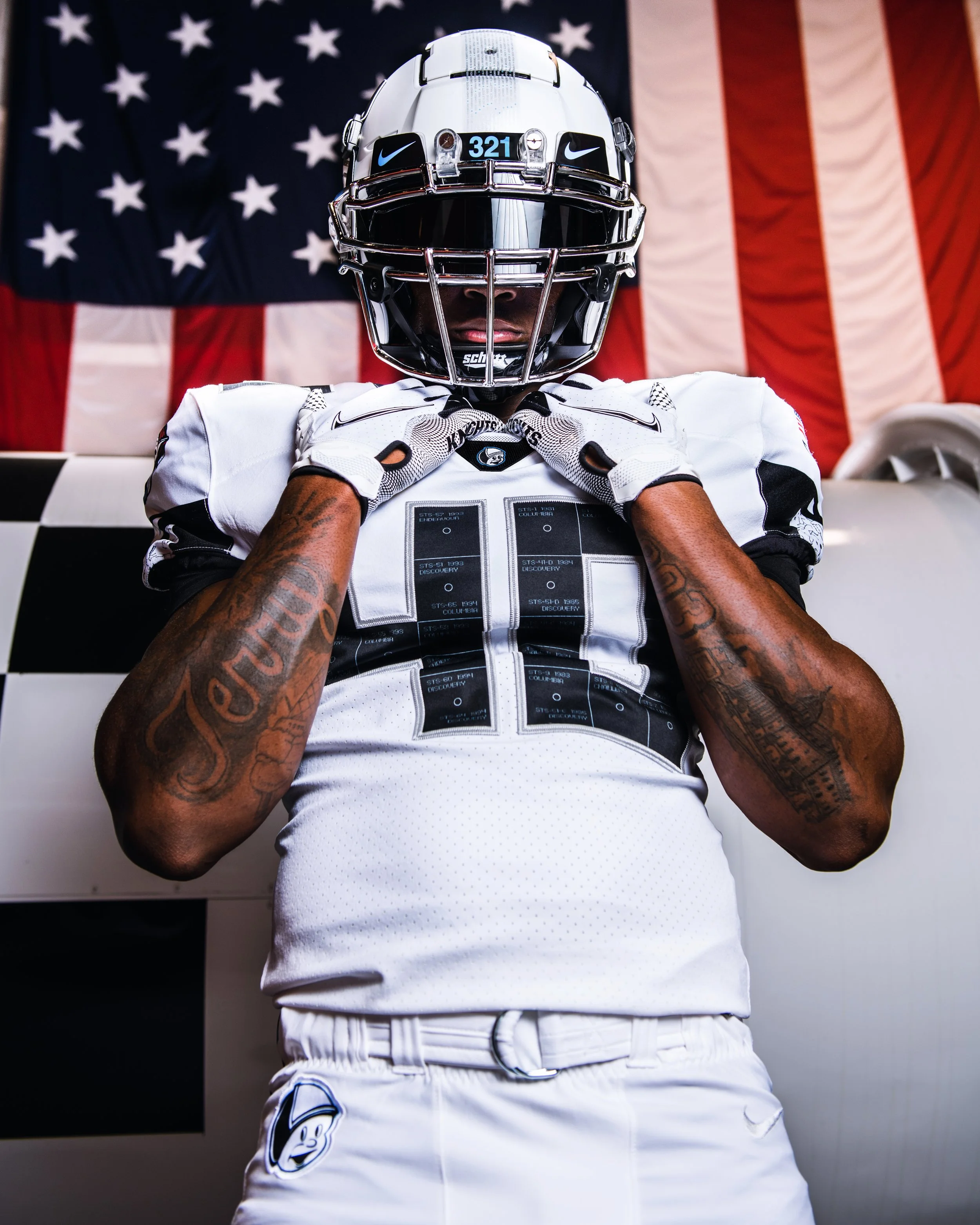 American football player in uniform and helmet standing in front of an American flag.