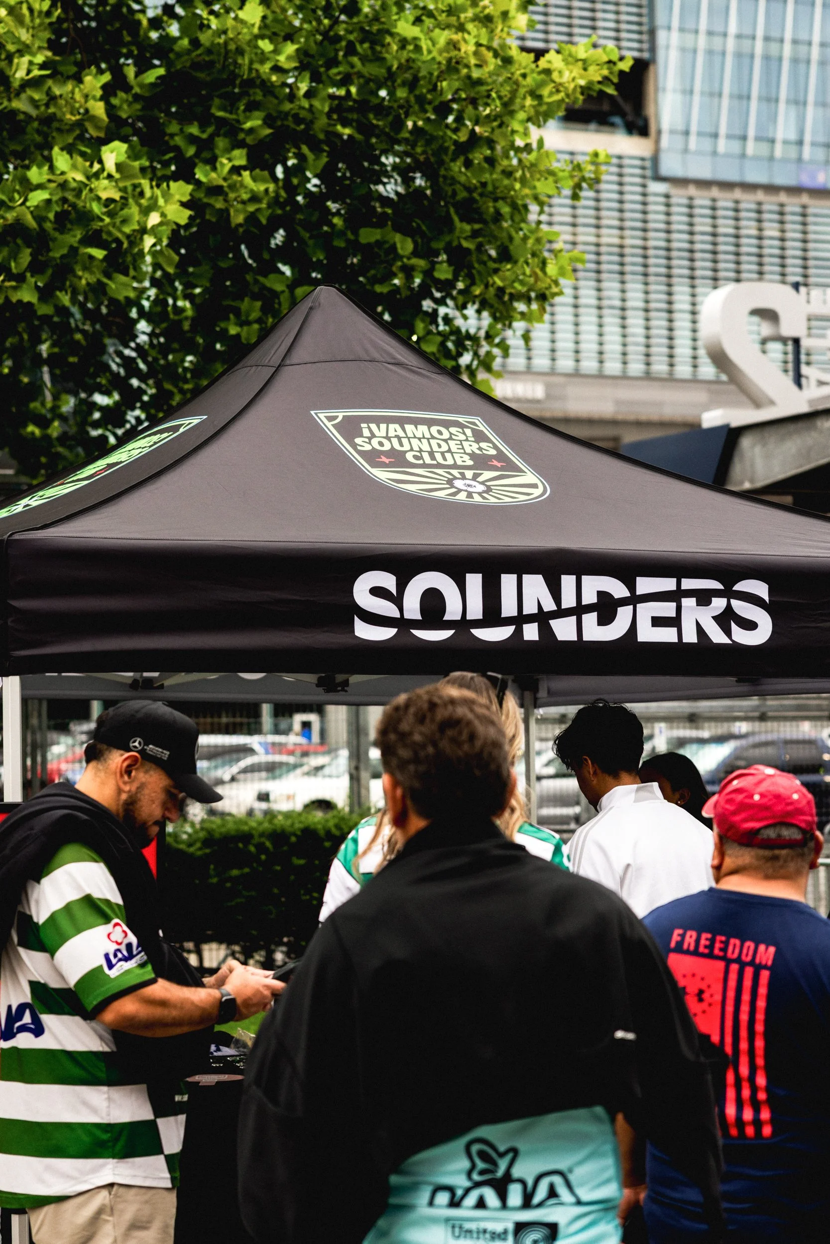 People gathered around a sounders club tent at an outdoor event.