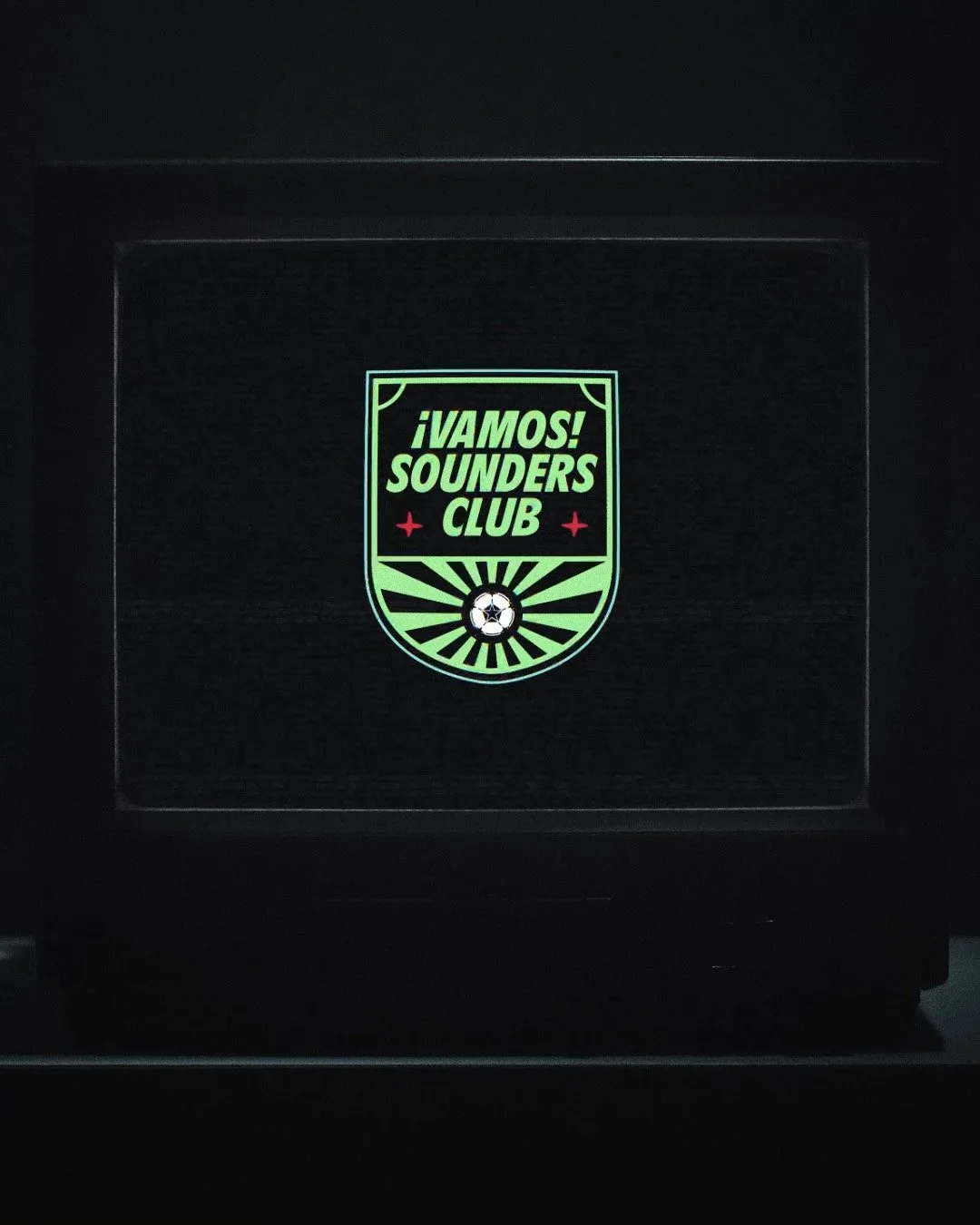 Lighted screen displaying a logo with the text "¡VAMOS! SOUNDER'S CLUB" and a soccer ball at the bottom, against a dark background.
