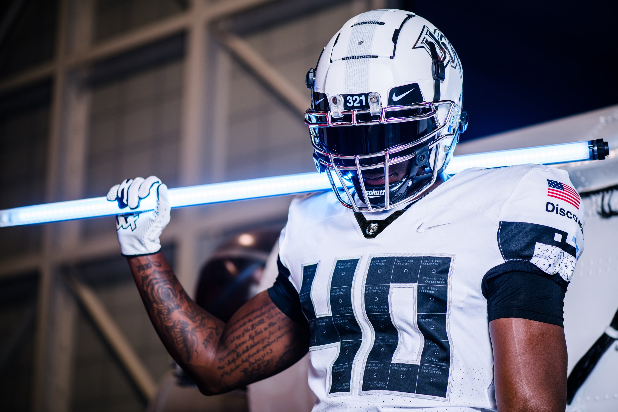 A football player in a white uniform and helmet, holding a glowing blue neon light rod.