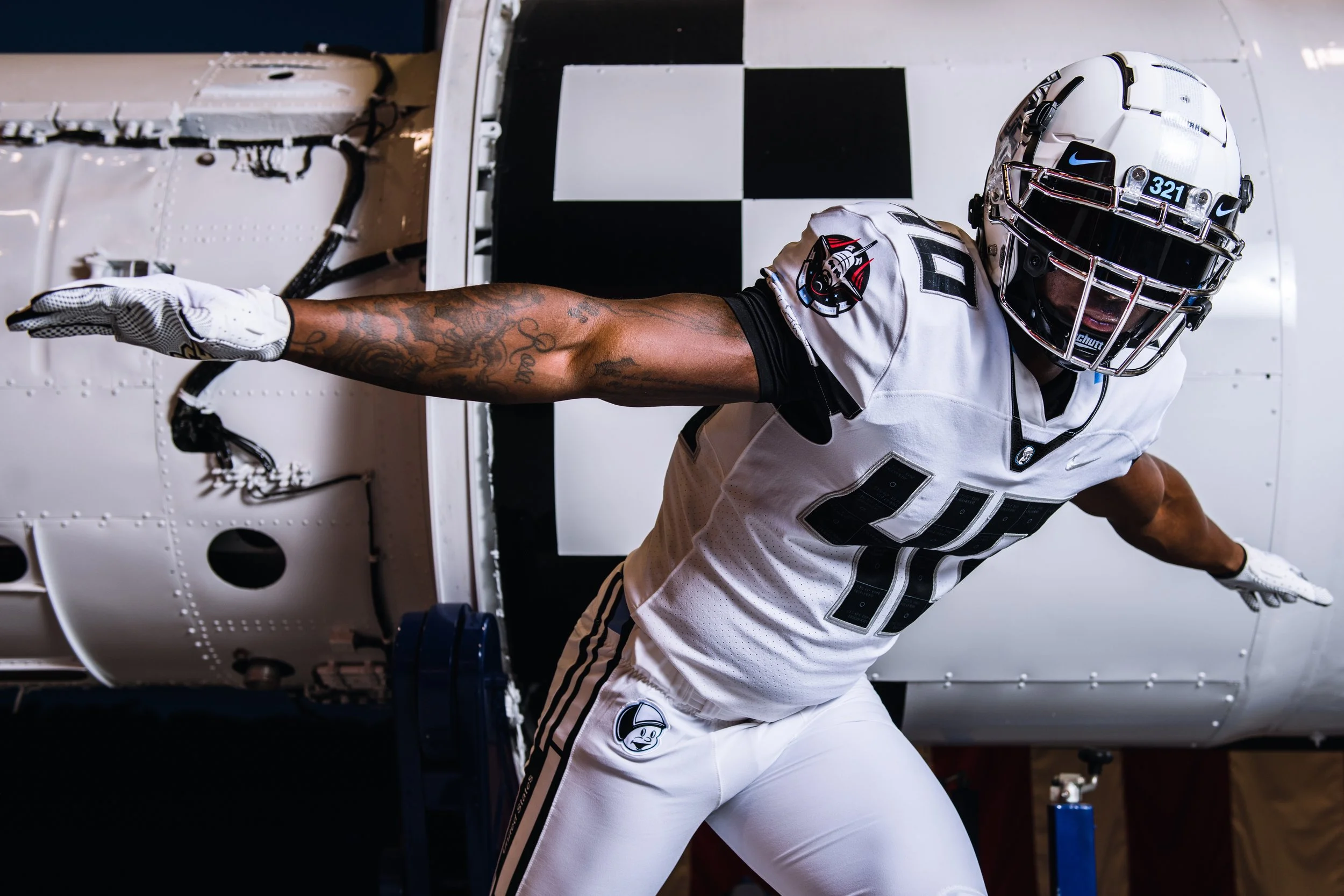 An American football player in a white uniform and helmet pushing against a wall inside a facility.