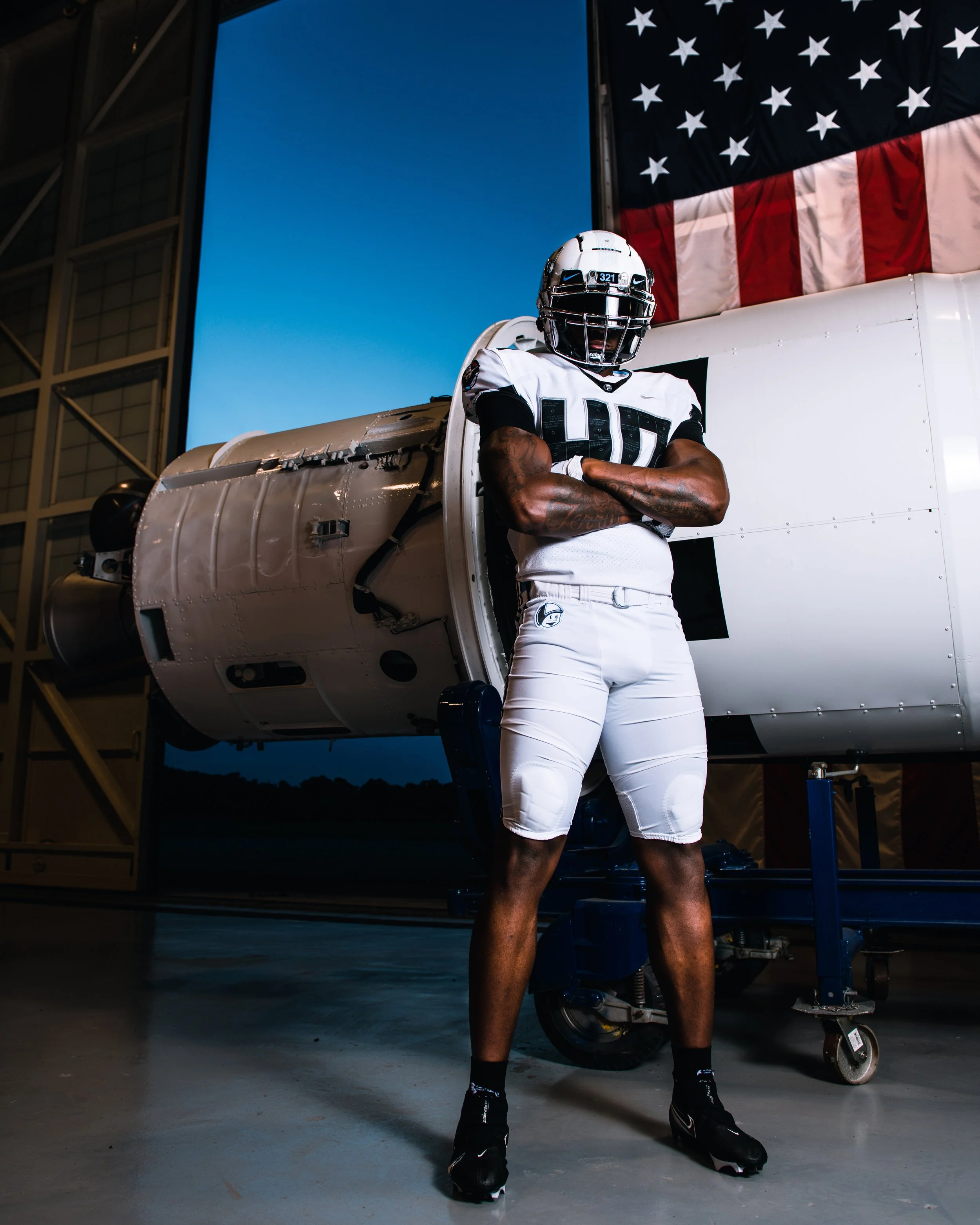 An American football player in uniform standing with arms crossed in front of a spacecraft.