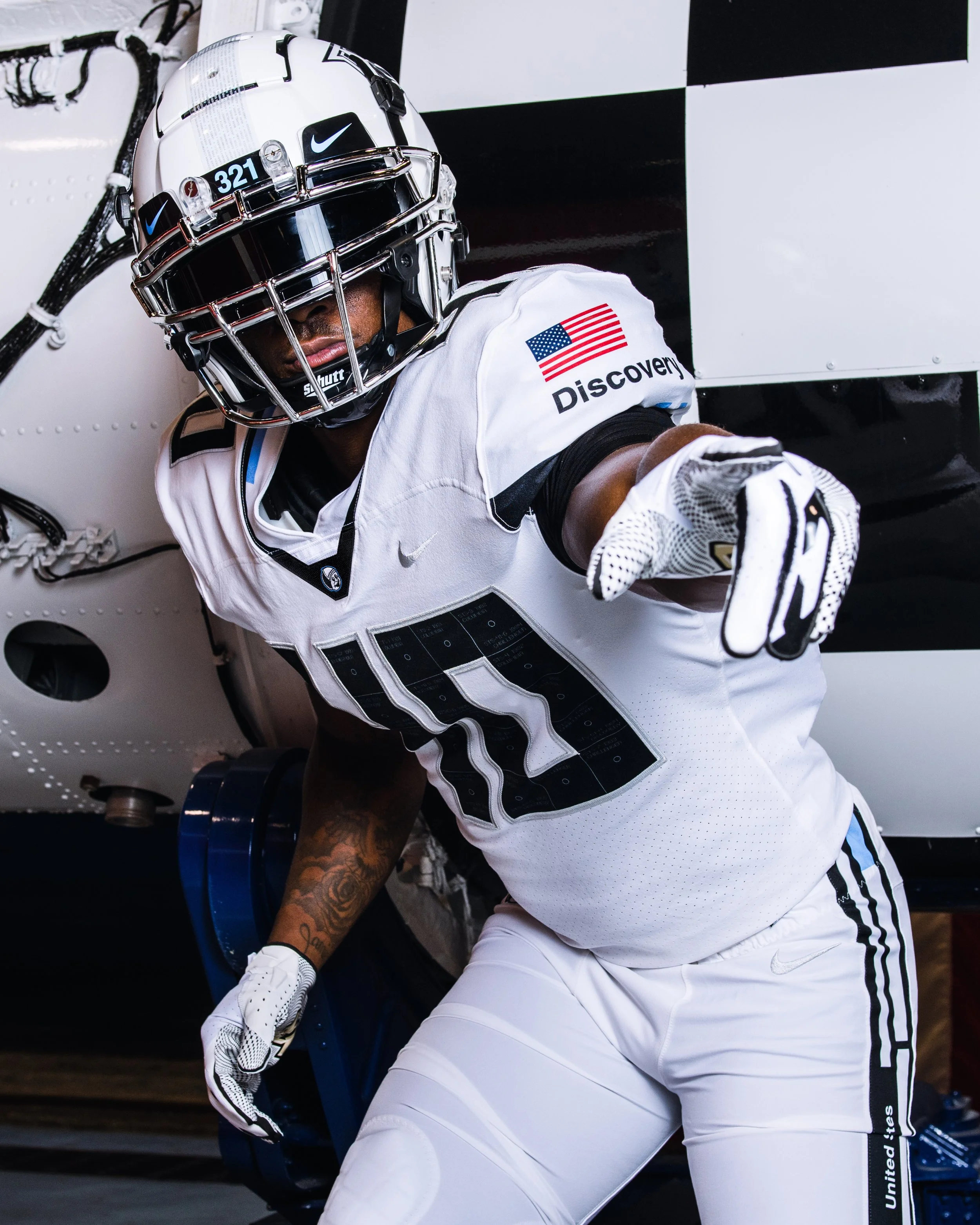 An American football player in a white uniform with black and gray details, wearing a helmet with a face mask, pointing forward.