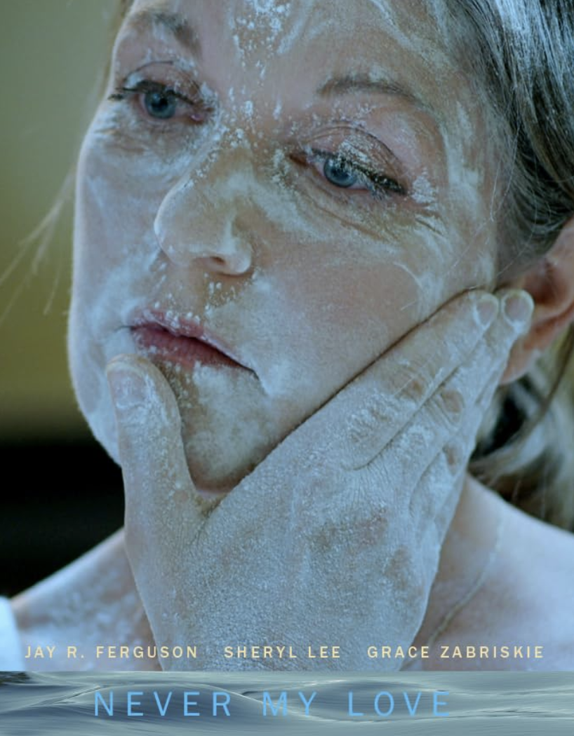 Close-up of a woman with blonde hair, blue eyes, and light skin, covered in white powder, with her hand touching her face.