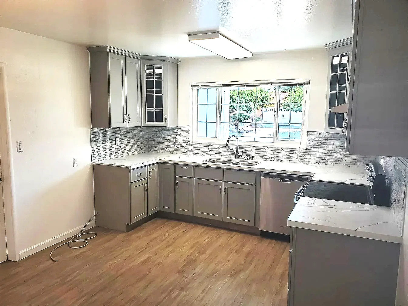 Kitchen with gray cabinets, white countertops, a large window above the sink, and hardwood floors.