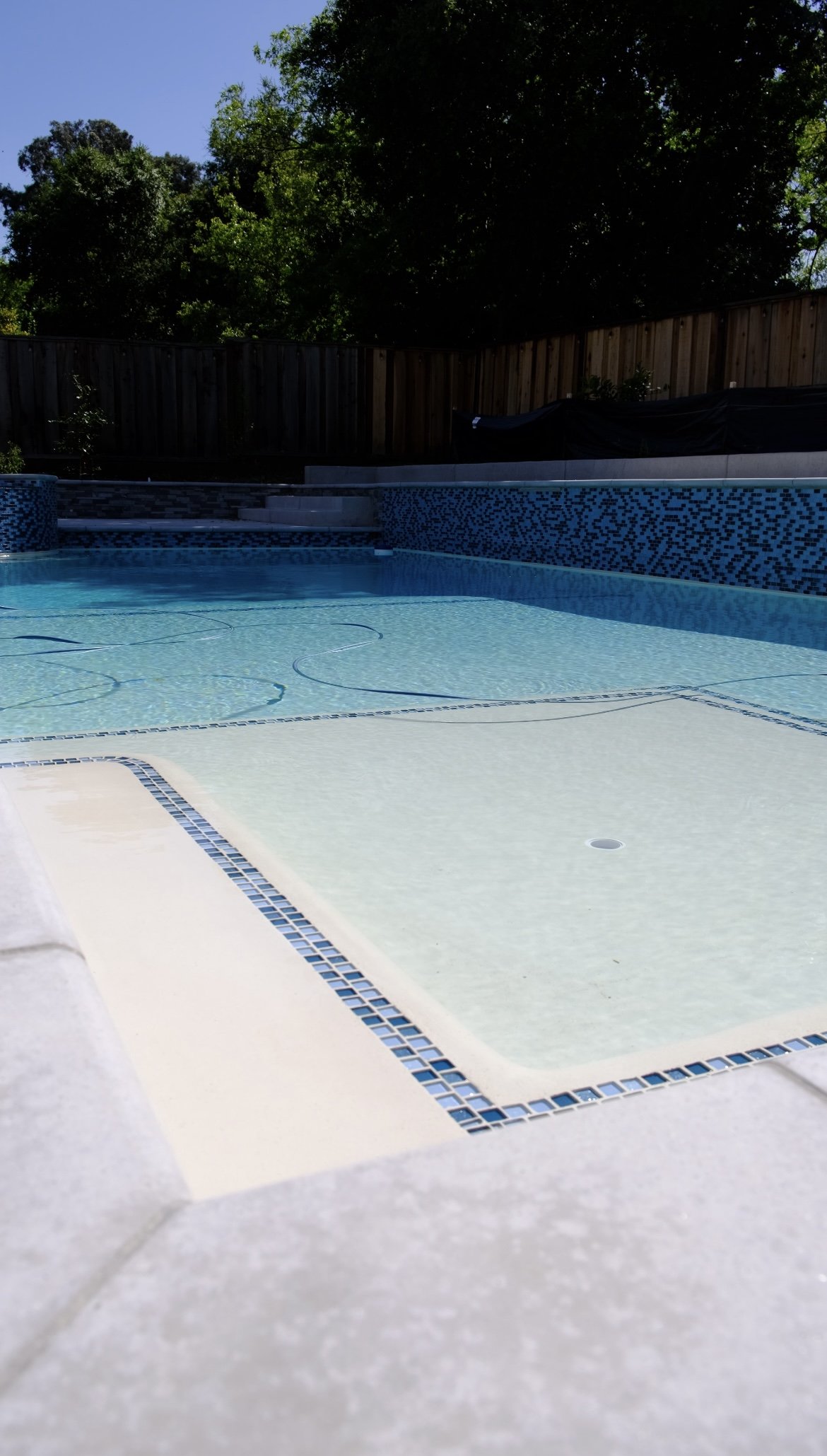 New swimming pool construction in San Ramon featuring a smooth white plaster finish and a custom Baja shelf with blue glass tile inlay by NorCal Pools Inc.