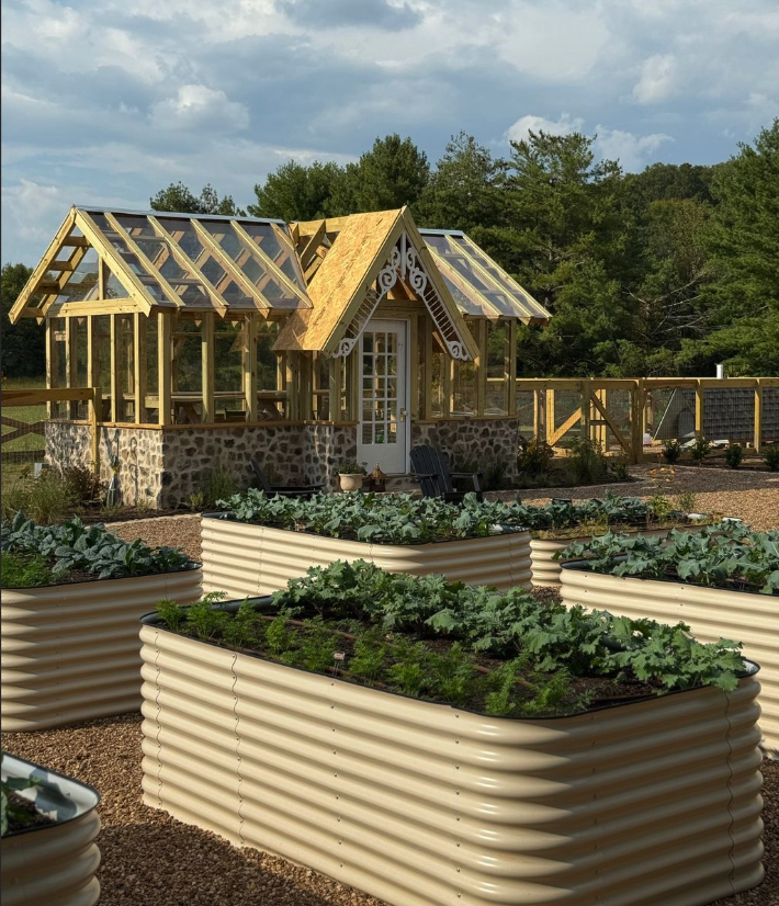 A backyard with raised garden beds and a small greenhouse with a glass roof and stone foundation.