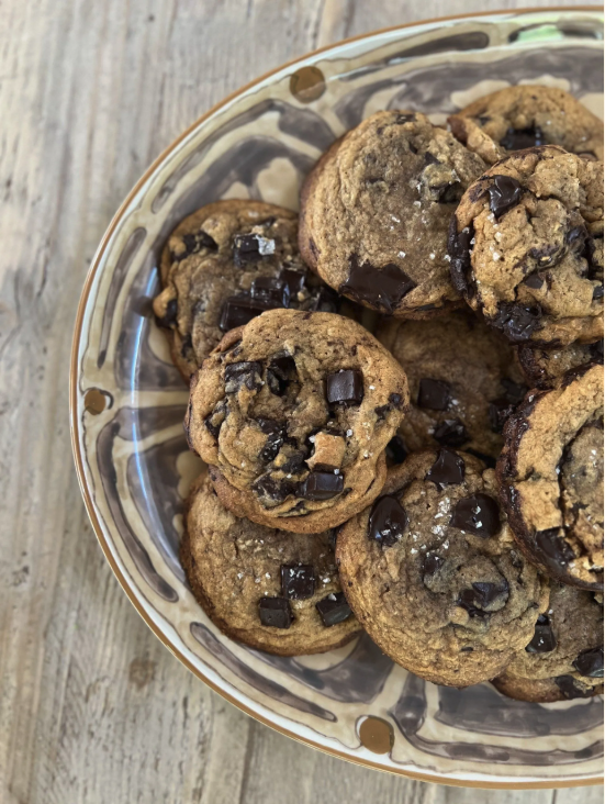 A glass bowl filled with chocolate chip cookies on a wooden surface.