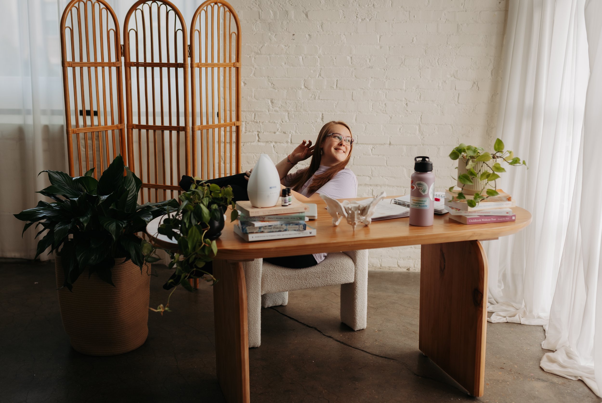 Brook + Brave Birth - Memphis, Tennessee Birth and Postpartum Doula sitting at a desk with childbirth education resources and labor comfort tools like a model pelvis, TENS unit and essential oil diffuser