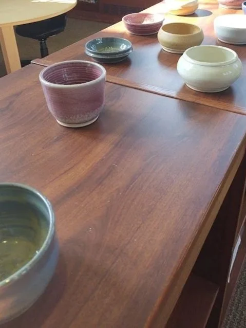 Various pottery bowls in different colors on a wooden table, with some bowls overlapping and others spaced apart.
