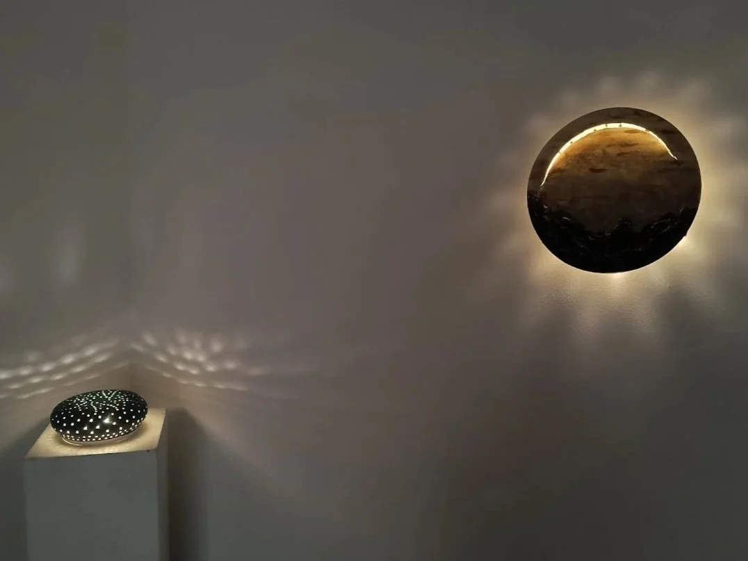 A black, round decorative object with white dots projecting starry patterns on the wall, and a mirror on the wall reflecting a landscape scene with a sunlit sky and mountains.