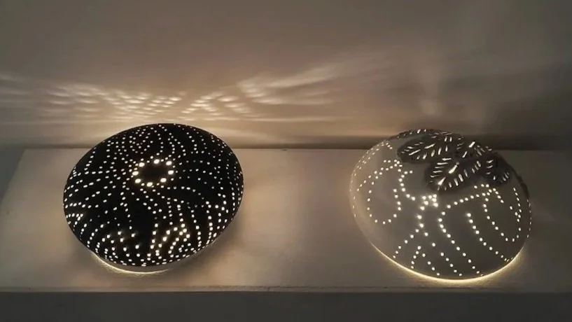 Two decorative spherical lamps with perforated patterns on a shelf, creating light and shadow effects on the wall above.