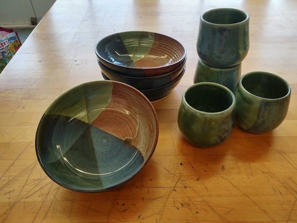 Set of ceramic bowls and cups with a green, brown, and black glazed pattern on a wooden table.