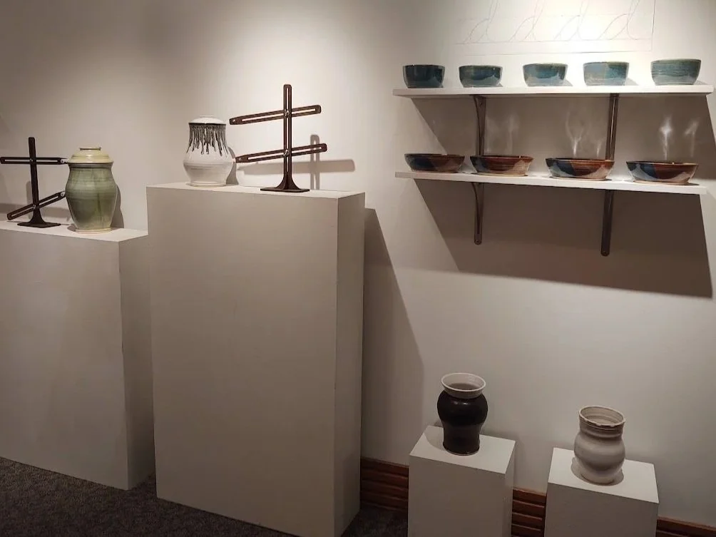 Display of various ceramic and pottery objects on white pedestals and wall-mounted shelves.