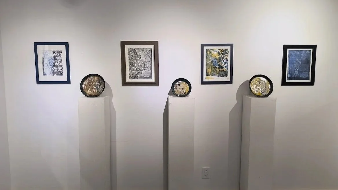 Gallery wall with five framed artworks and three circular decorative objects on white pedestals.