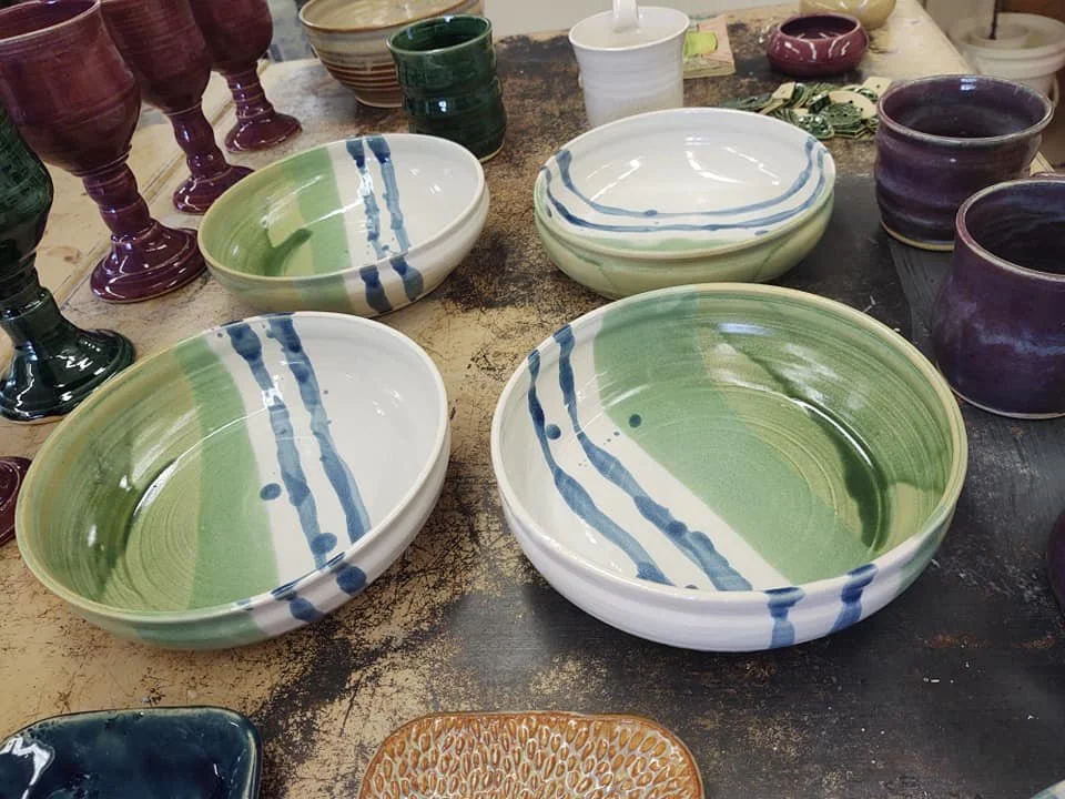 Various ceramic bowls and glasses in different colors and sizes arranged on a rustic wooden table.