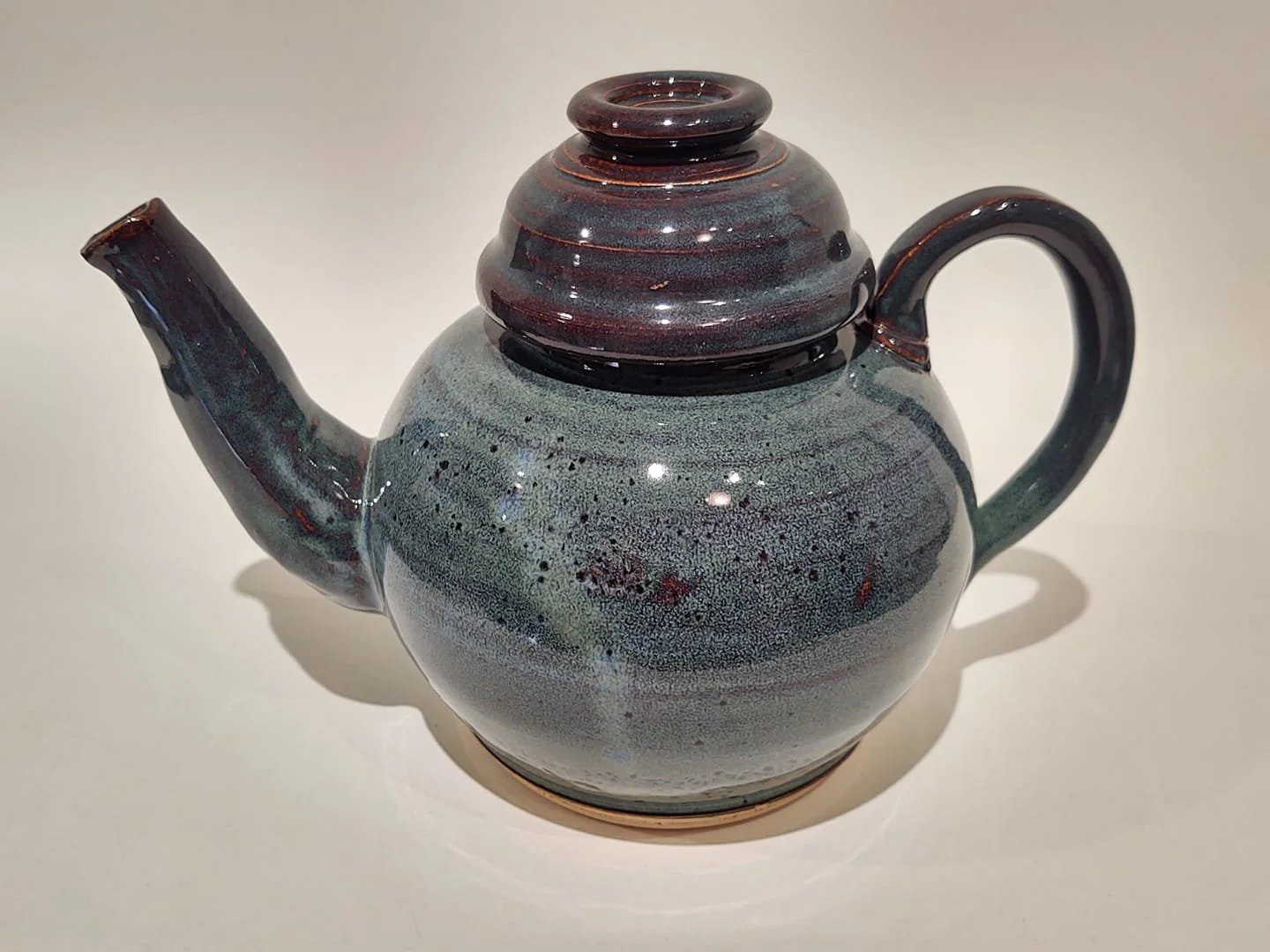 Ceramic teapot with a rounded body, a short spout, a handle on the side, and a lid on top, set against a plain light background.