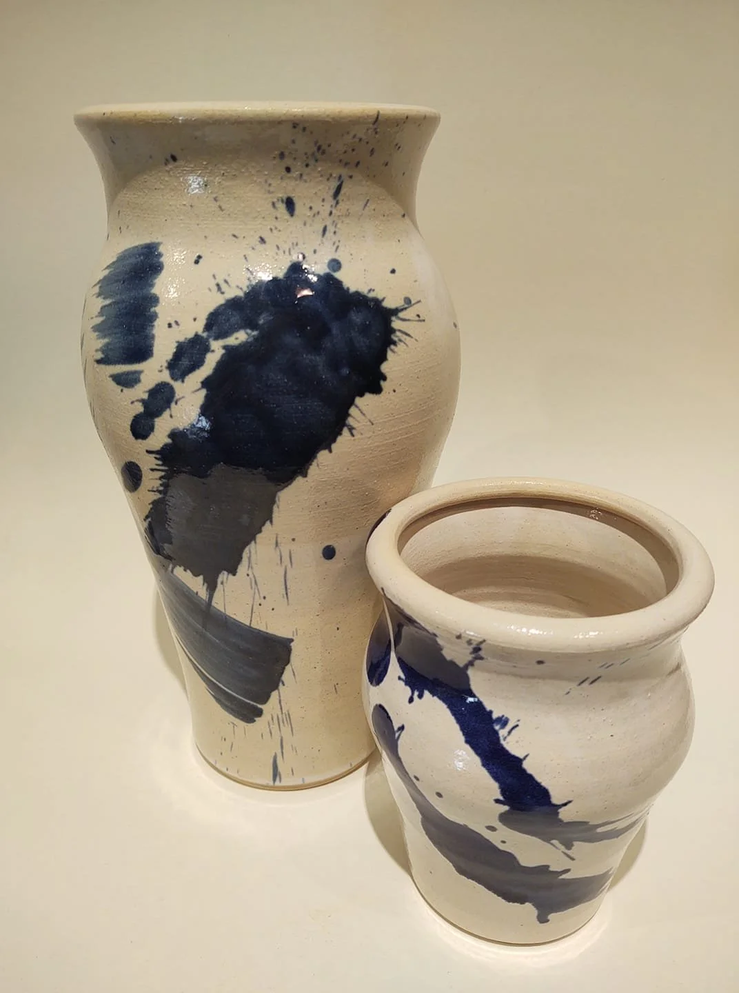 Two ceramic vases with abstract blue and black paint splatter patterns on a light background.
