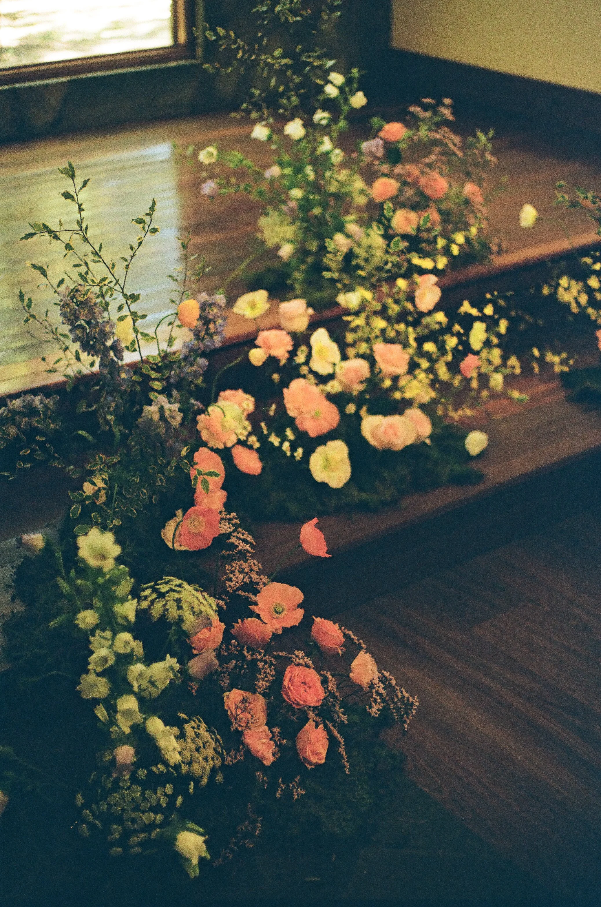 A floral arrangement with pink, white, and purple flowers on a wooden surface near a window.