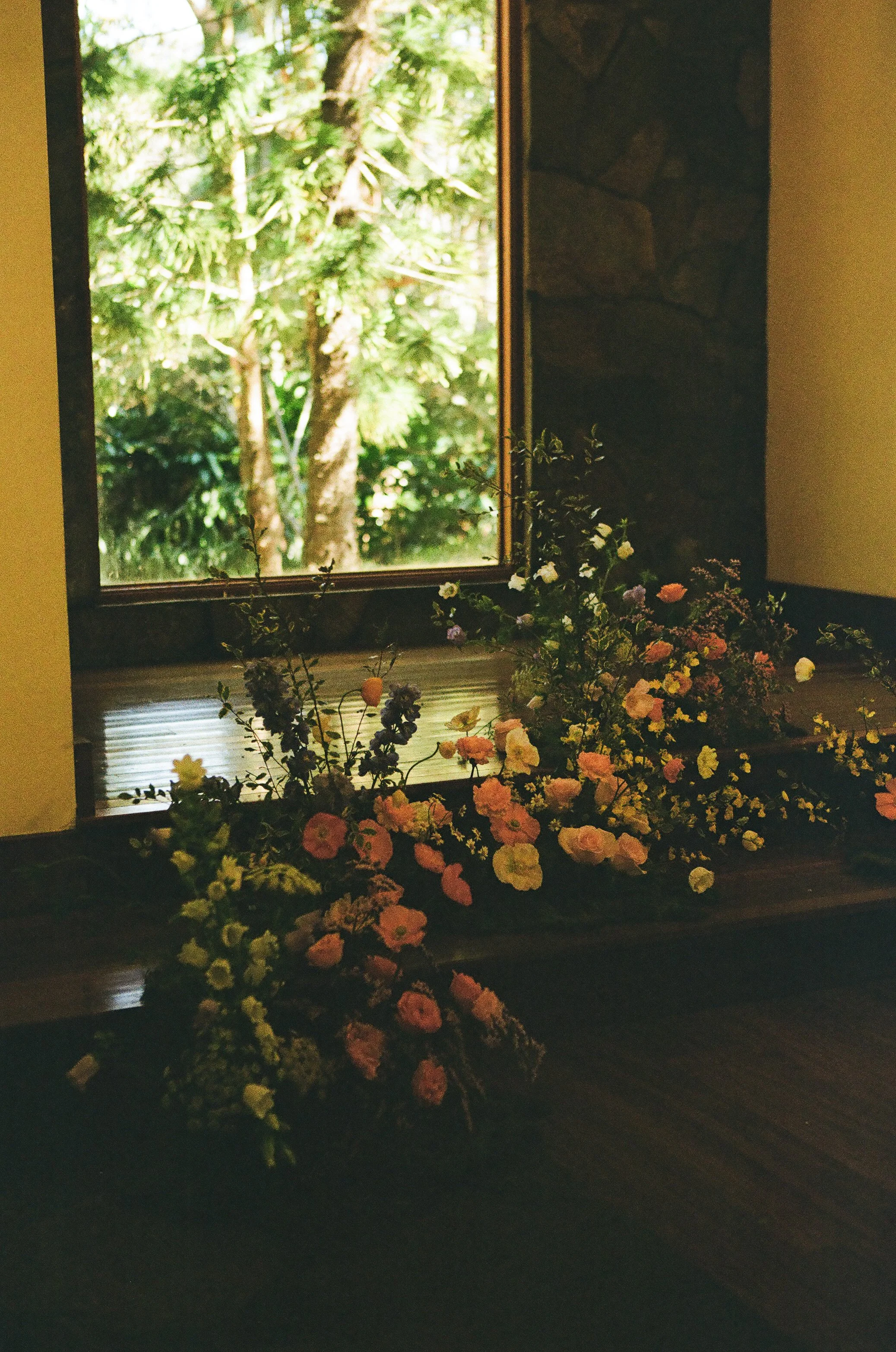 A window with a view of lush green trees, and a wooden ledge below the window decorated with colorful flowers.