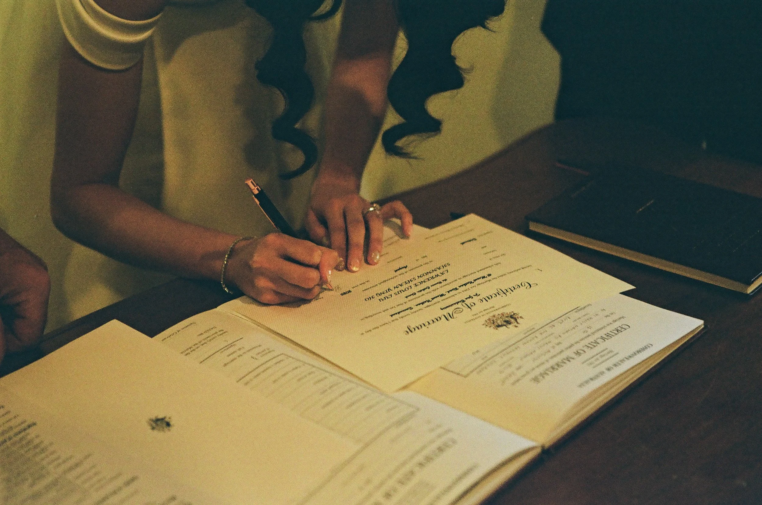 Person signing an official document at a desk with books and papers.