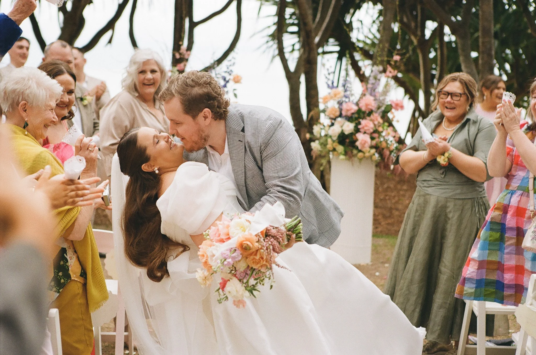 A newlywed couple dances at their wedding while surrounded by joyful guests outdoors.