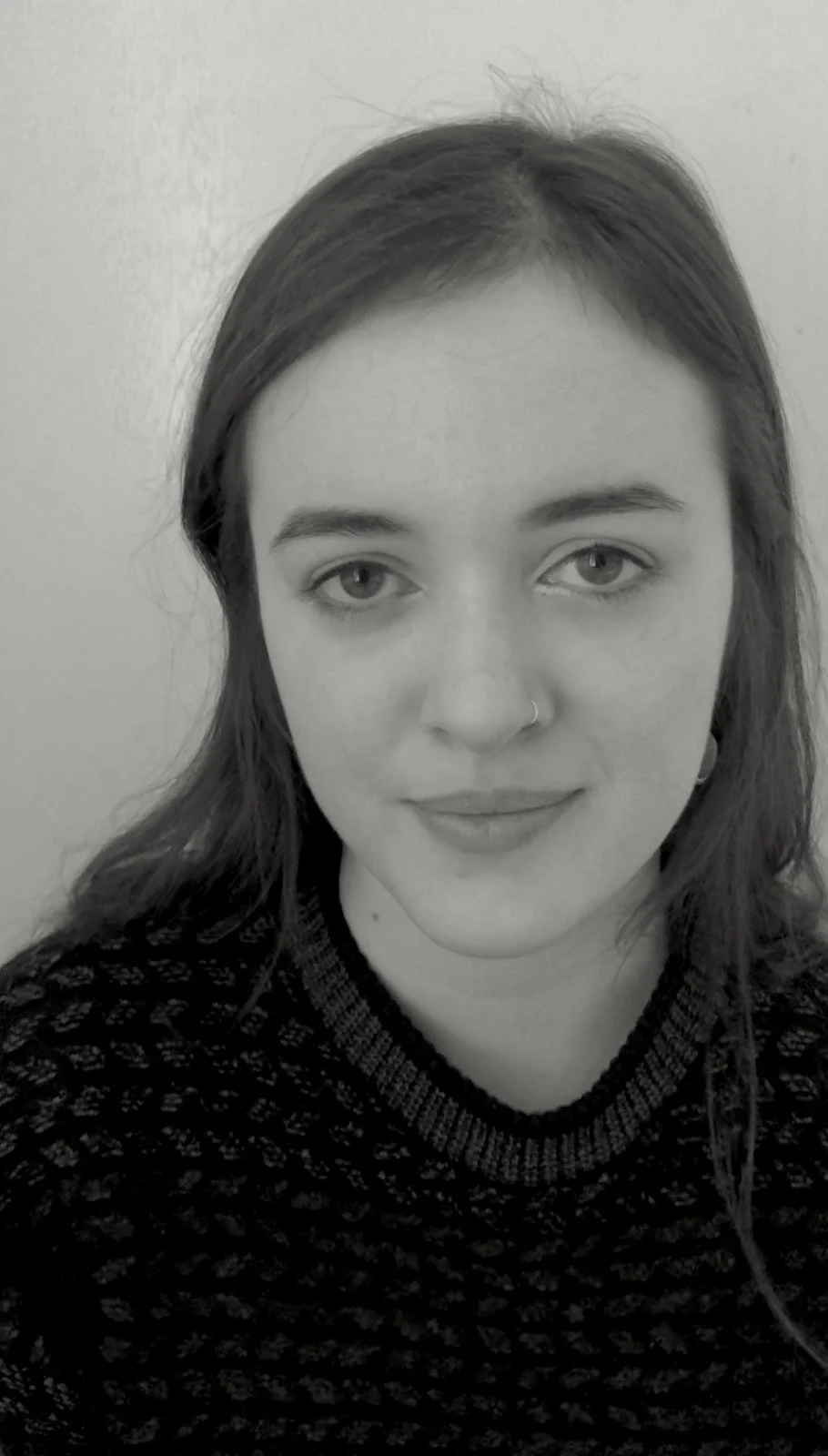 A young woman with medium-length hair, wearing a patterned sweater and a nose ring, looking at the camera.