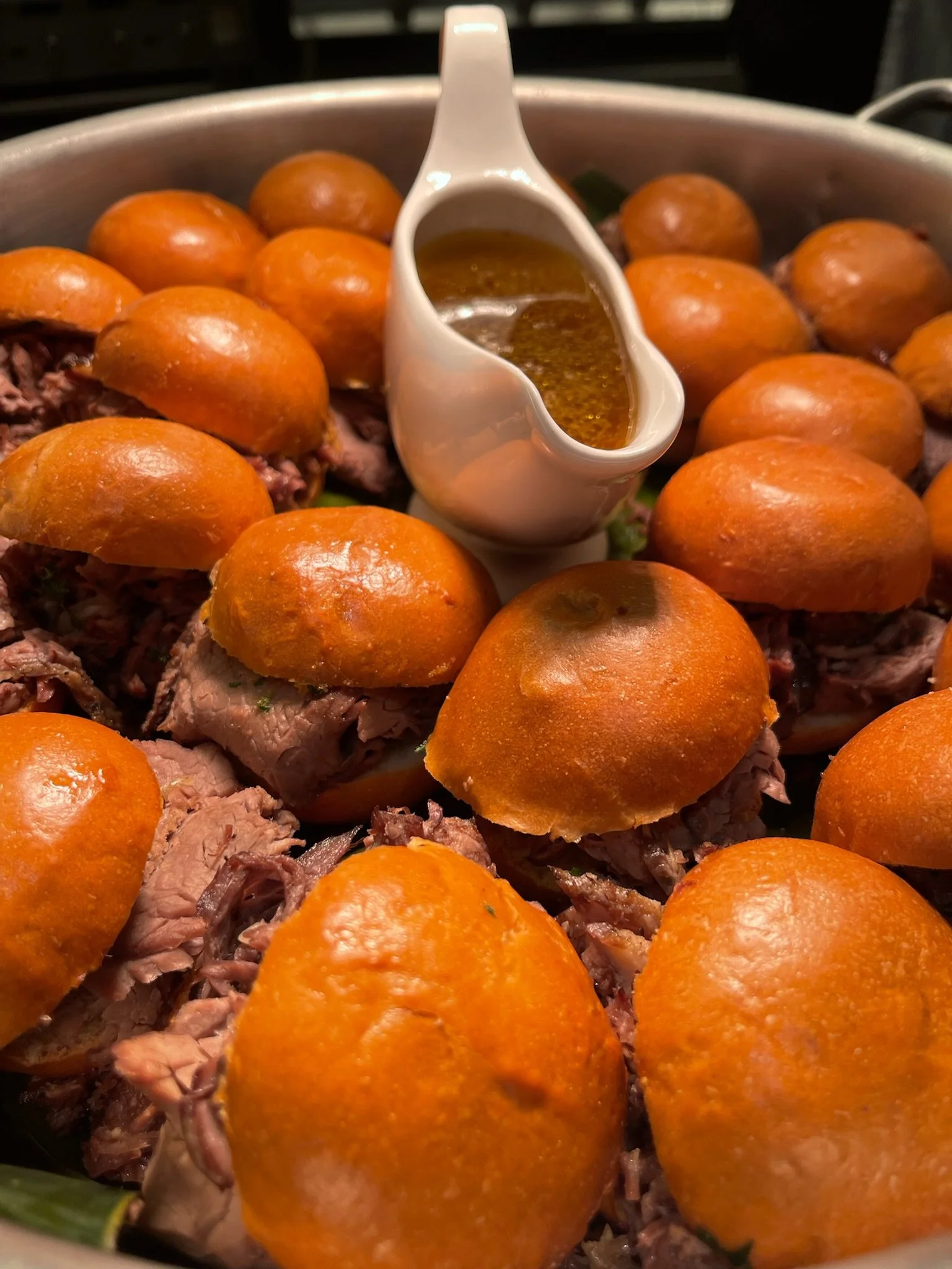 A tray of cooked meat topped with small, round, golden-brown bread rolls and a white gravy boat filled with gravy in the center.
