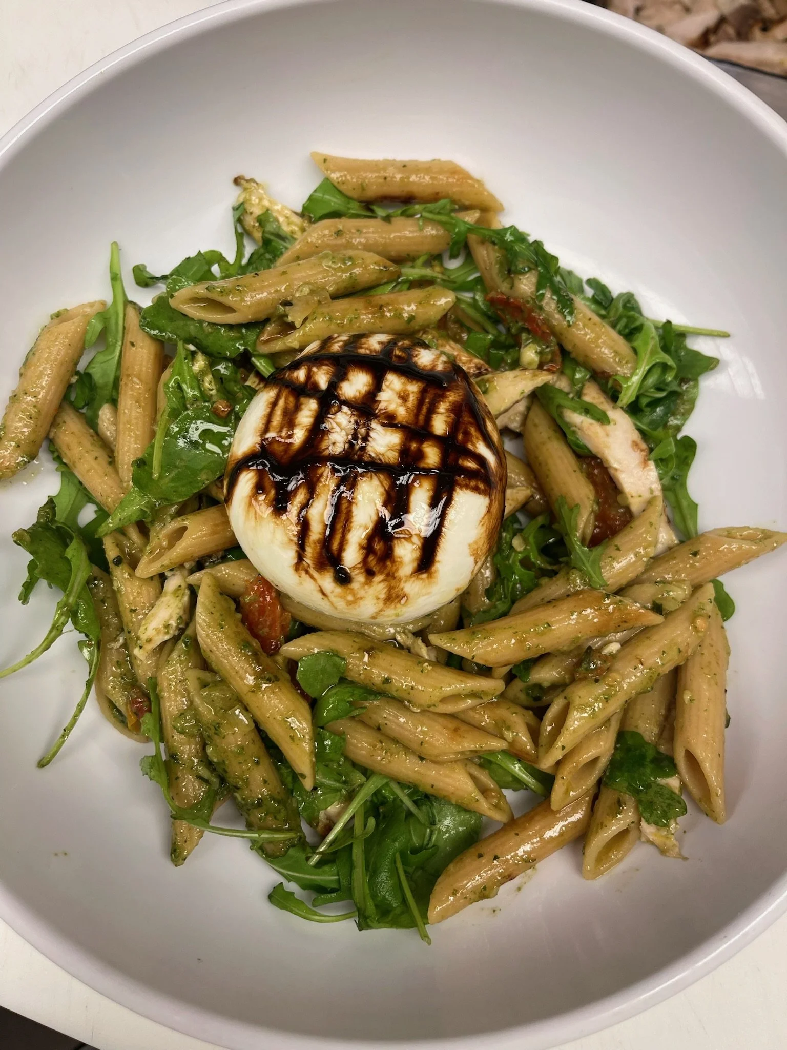 Pasta salad with greens and a topped soft-boiled egg drizzled with balsamic glaze