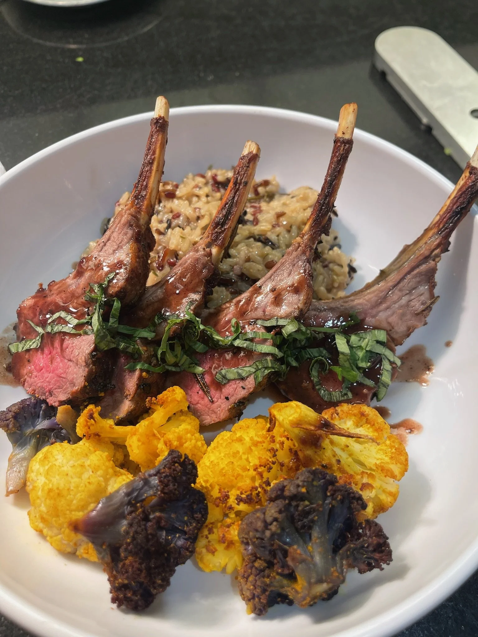 Lamb chops garnished with herbs, served with roasted cauliflower and a side of rice with vegetables.