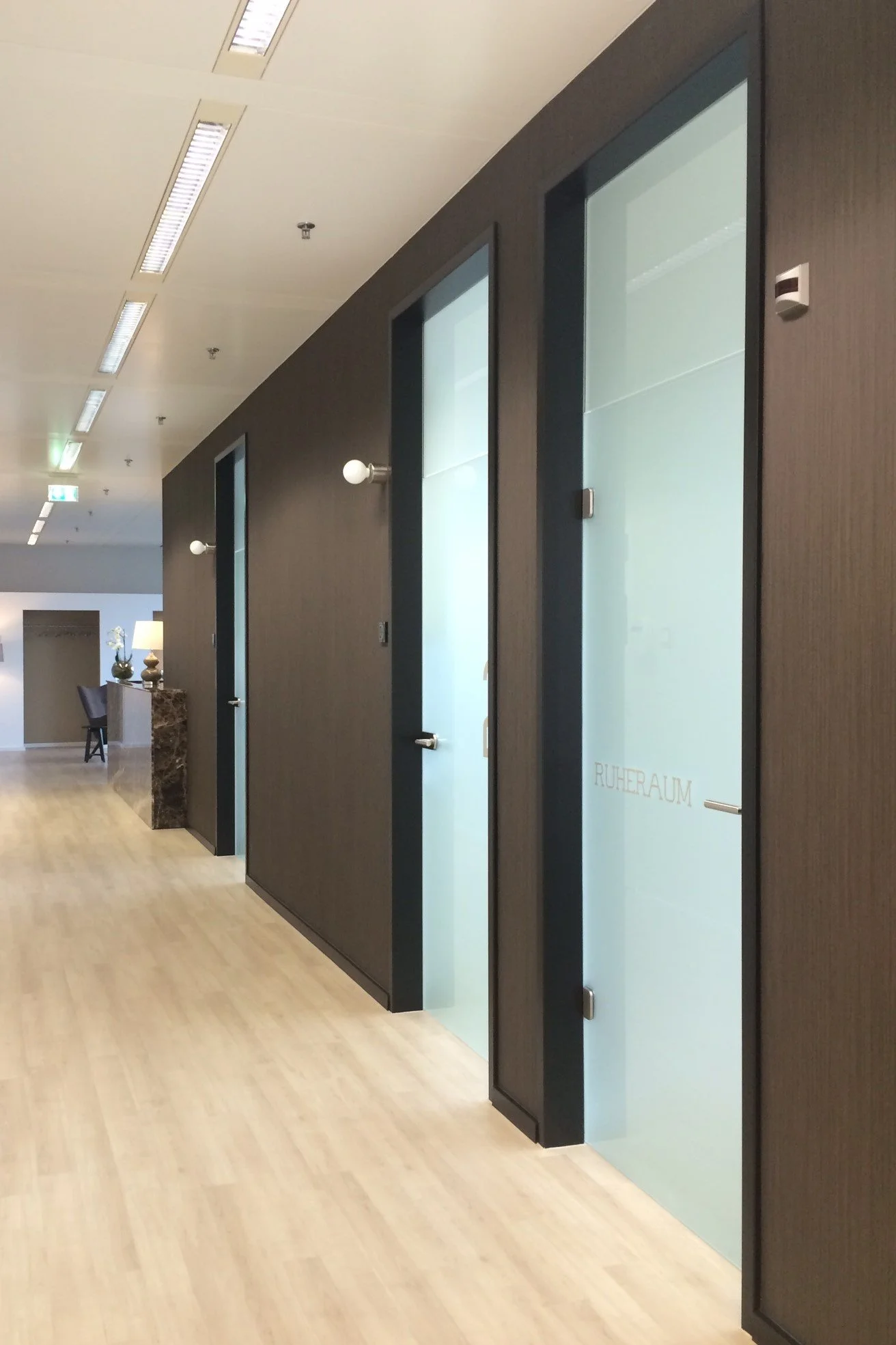 Innenansicht eines Flurs mit schwarzen Wänden und Glas-Türen, eine Tür ist mit der Beschriftung 'RUHERUAM' versehen.