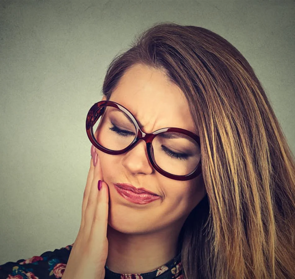 Frau hält sich die schmerzende Wange wegen verspannter Kaumuskulatur und Kieferschmerzen durch CMD