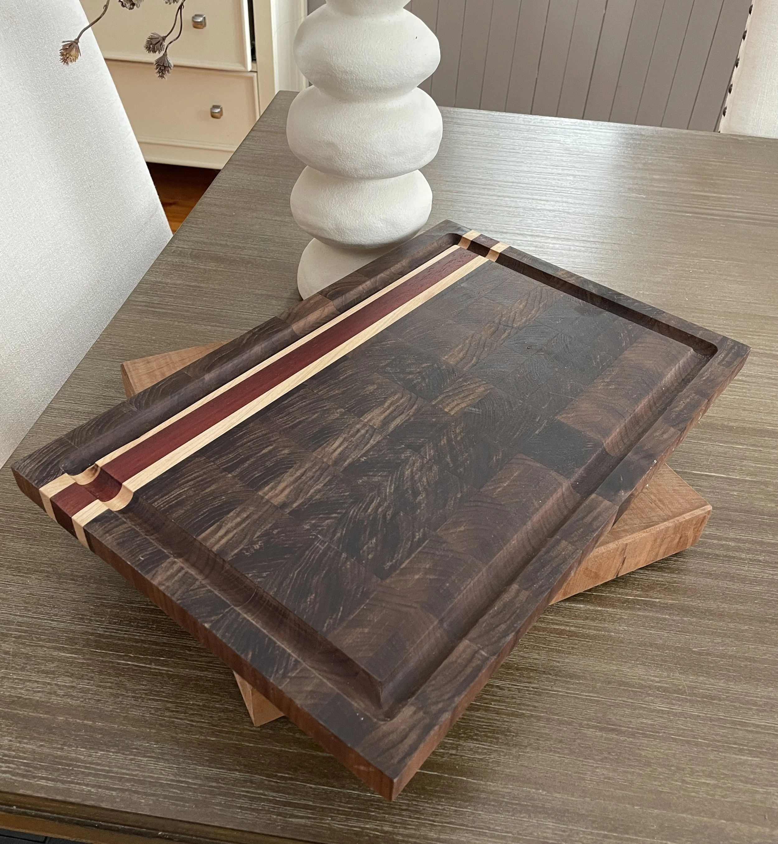 A wooden cutting board with a dark wood grain pattern and a decorative striped inlay.