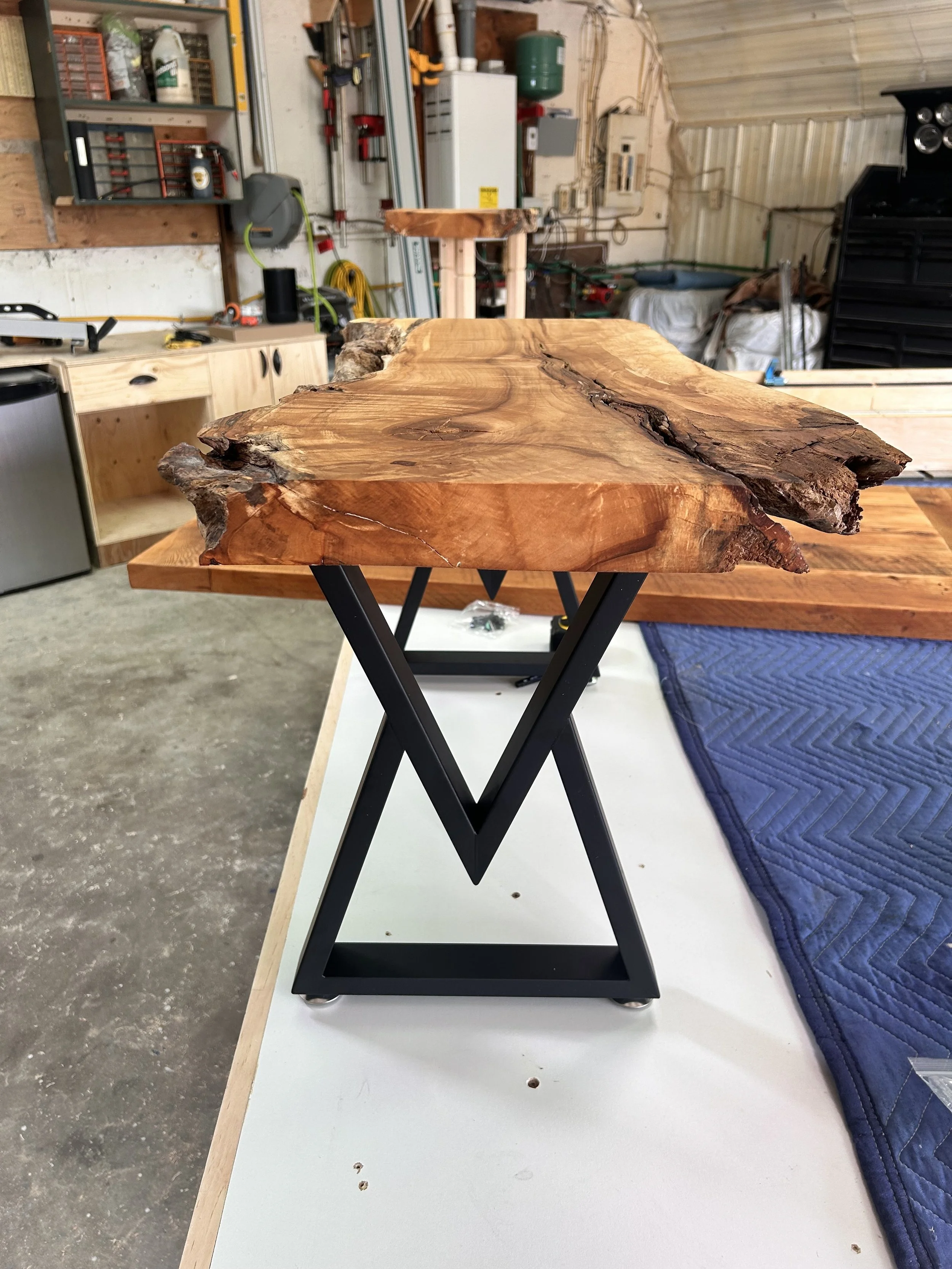 Live edge wooden table top on a black metal stand in a workshop.