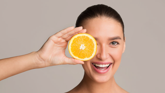 Smiling woman holding half of an orange up to her eye