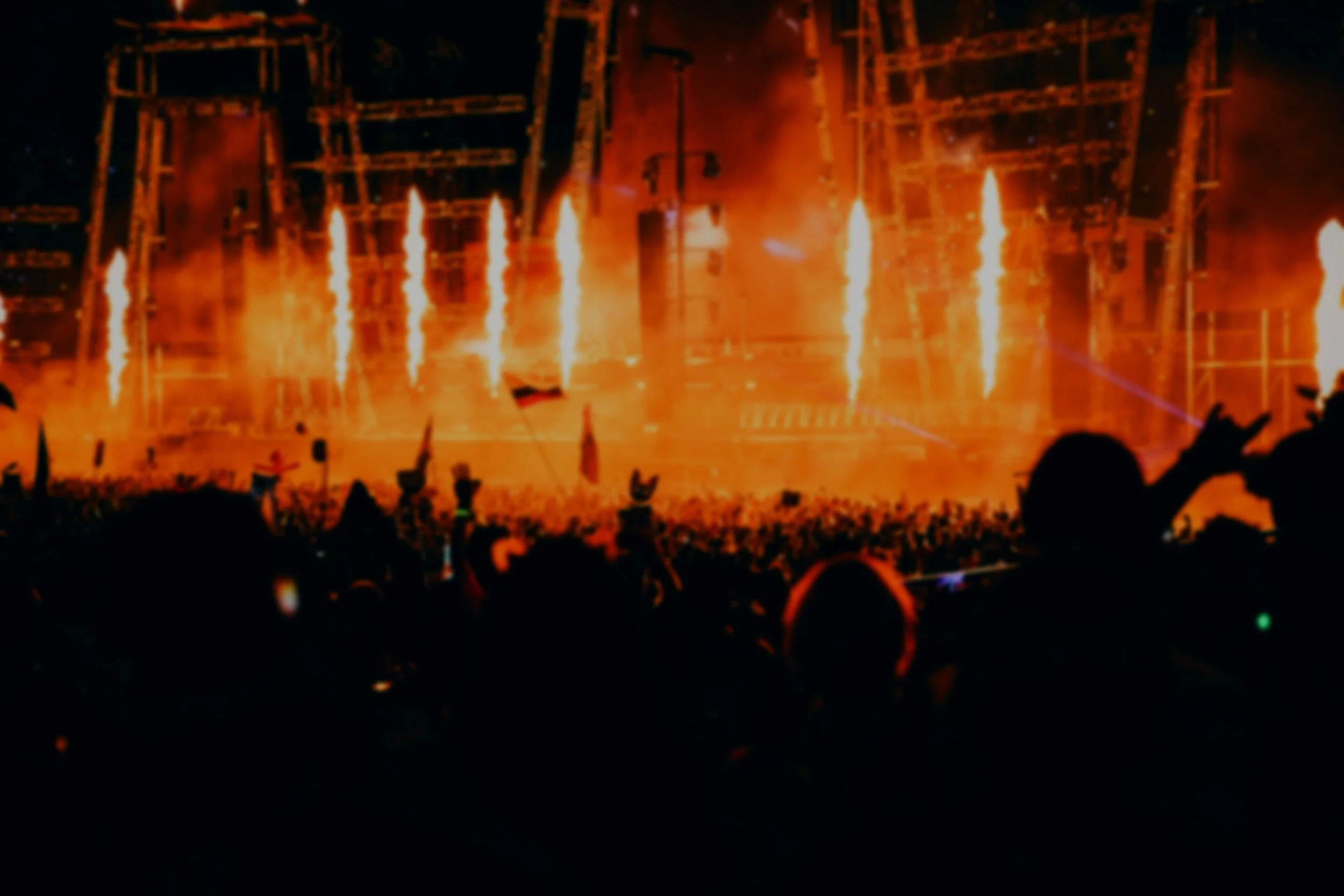 A fire show featuring multiple streams of fire shooting upward against a dark background, with silhouettes of a crowd at the bottom.