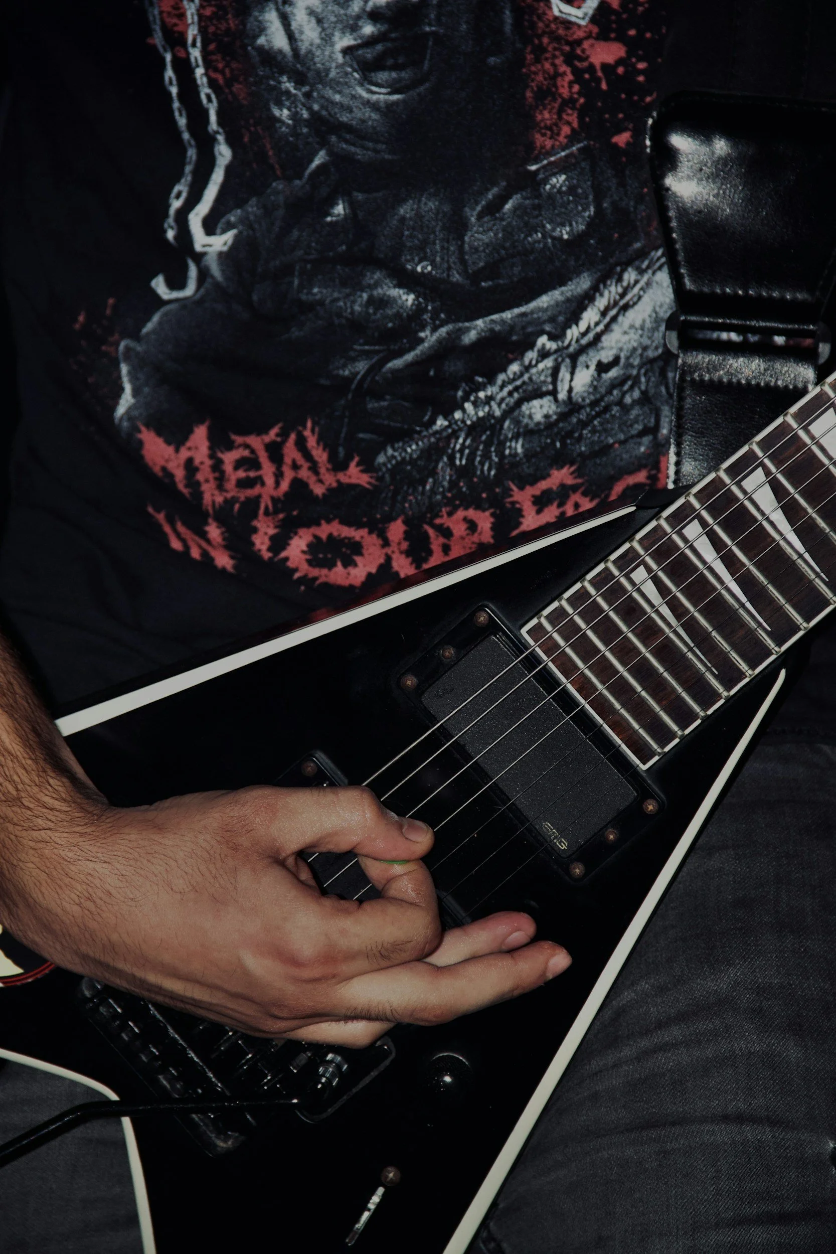 Person playing an electric guitar while sitting on a black and white surface, wearing a black shirt, and a shirt with a graphic print.
