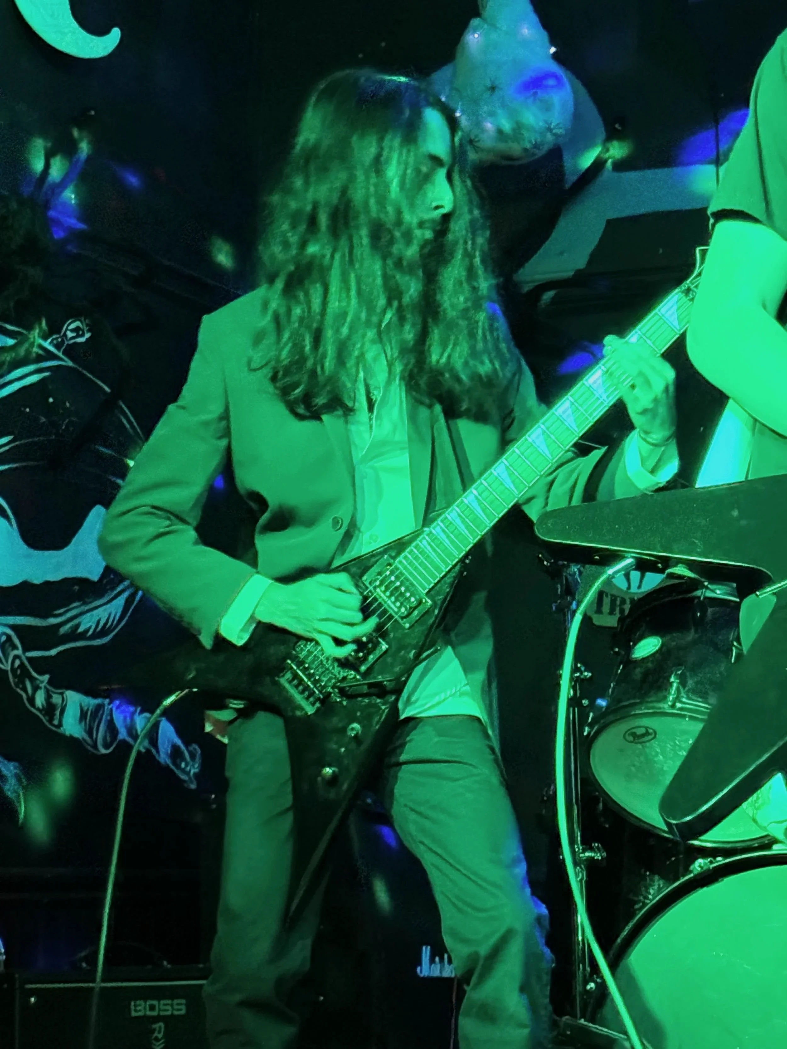 Aidan is playing the electric guitar on stage under green and blue stage lighting.